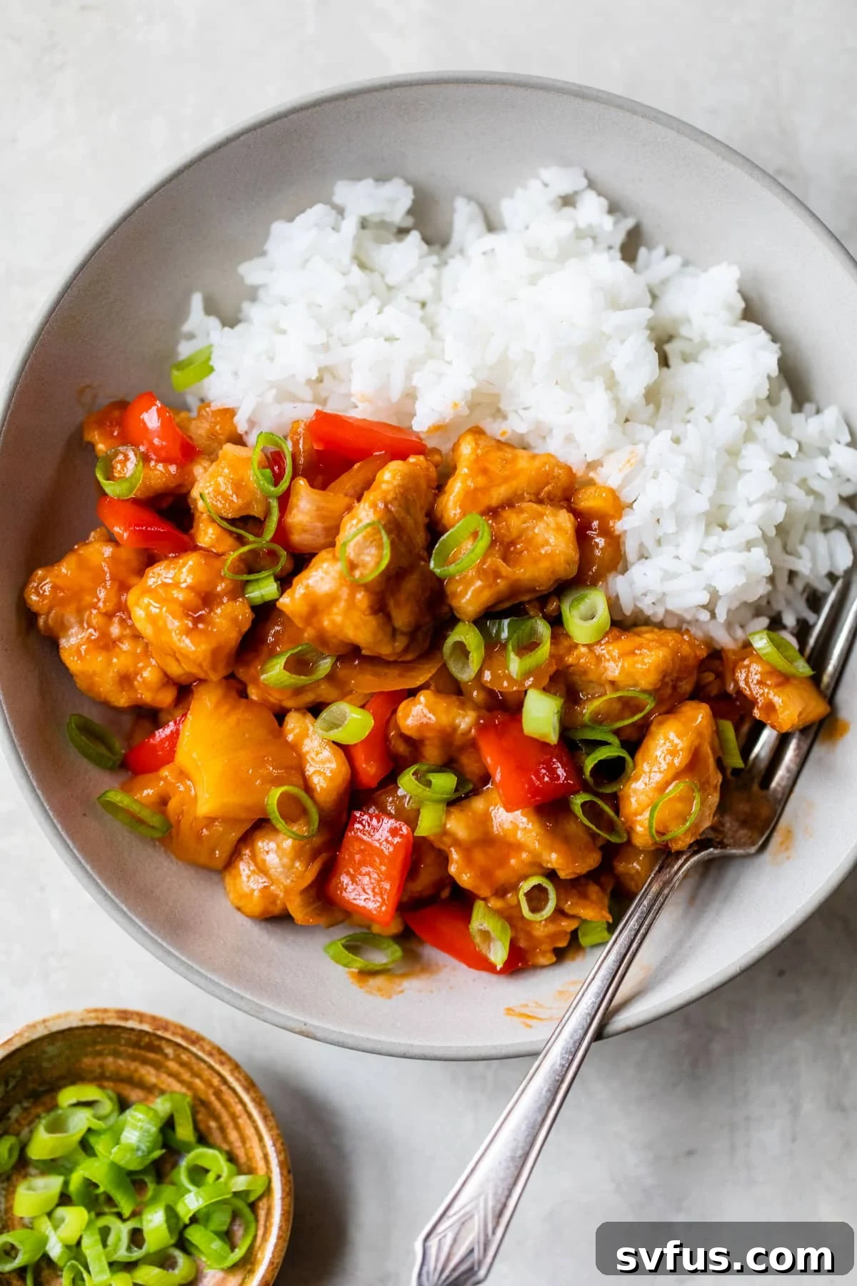 A satisfying bowl of fluffy rice topped with vibrant, healthy sweet and sour chicken, garnished with fresh herbs.