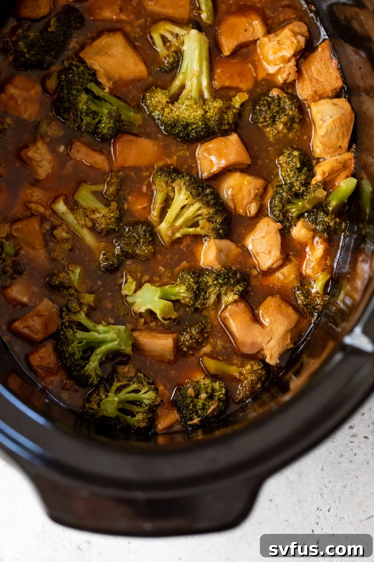 Tender broccoli florets and succulent chicken pieces bathed in a vibrant orange sauce, simmering gently in a slow cooker.