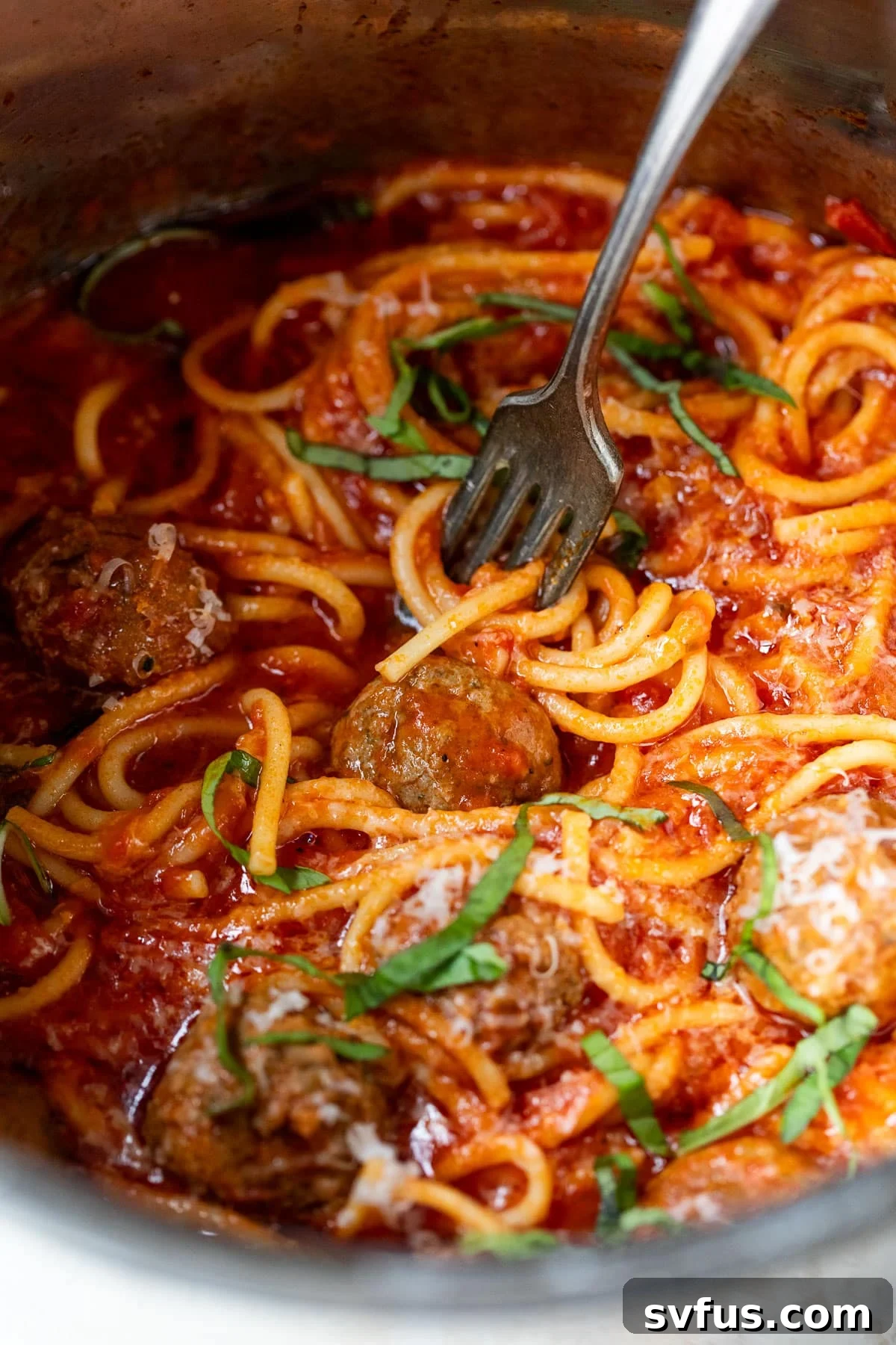 Close-up shot of a fork twirling spaghetti and meatballs in a rich red sauce, directly in the Instant Pot liner.