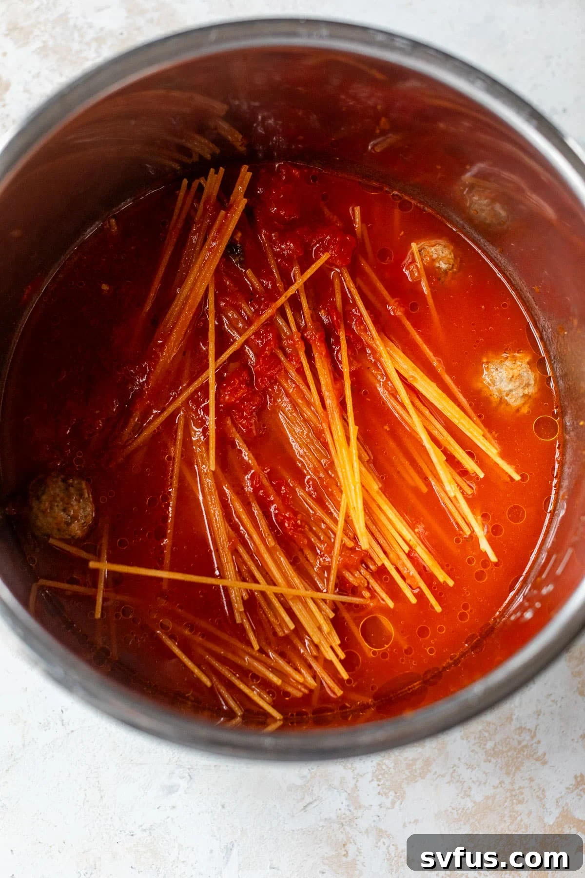 Overhead view of uncooked spaghetti noodles, frozen meatballs, and marinara sauce layered inside an Instant Pot, ready for cooking.