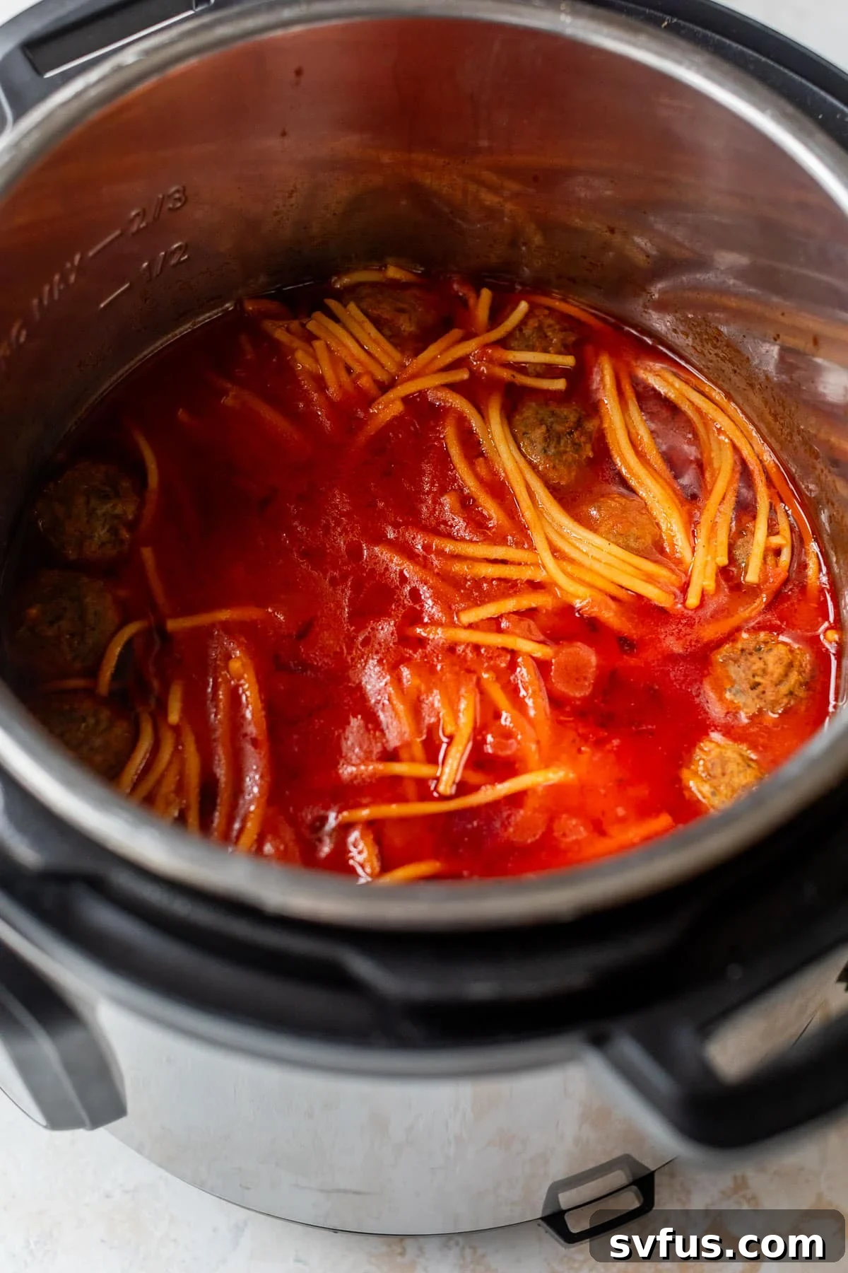 Side view of perfectly cooked spaghetti and meatballs simmering in rich tomato sauce inside the Instant Pot liner.