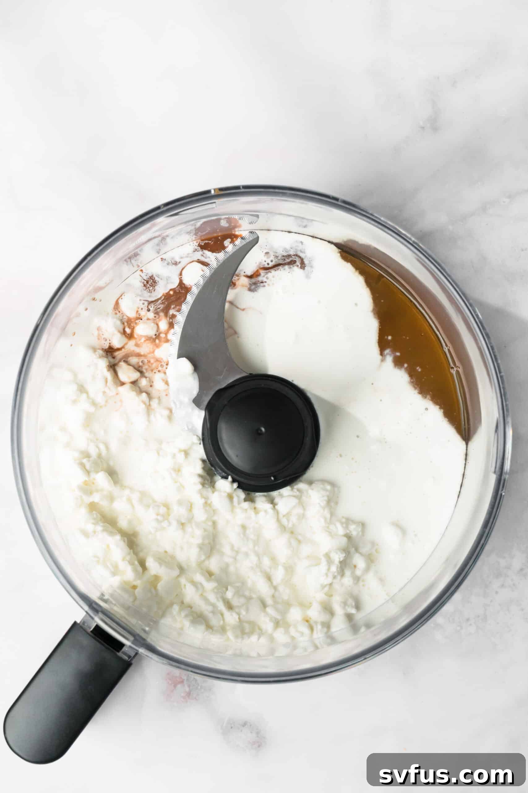 Overhead view of the wet ingredients for cottage cheese cookie dough in a food processor.