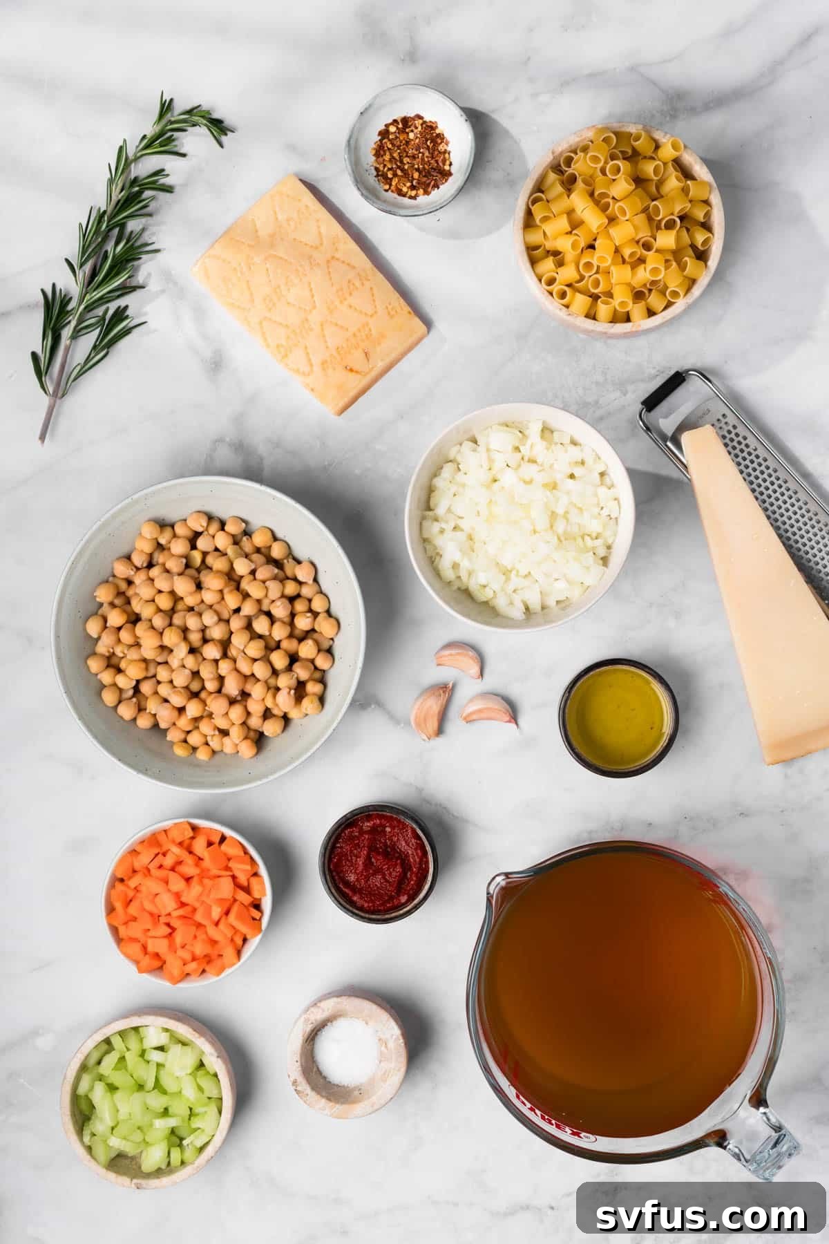 Overhead view of all the fresh ingredients for Pasta e Ceci laid out in individual bowls: diced vegetables, pasta, chickpeas, herbs, and Parmesan.