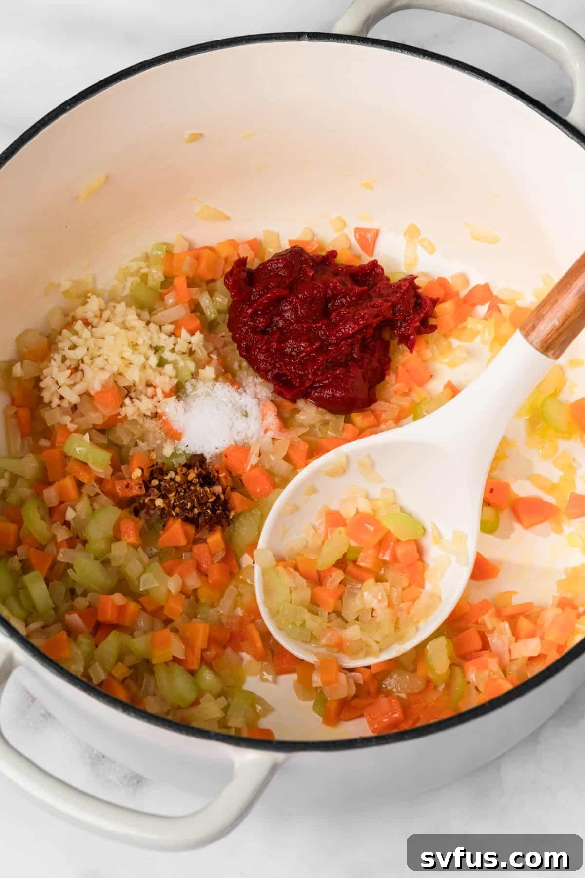 Overhead view of a white spoon stirring cooked onions, carrots, and celery in a pot for the soffritto base of Pasta e Ceci.