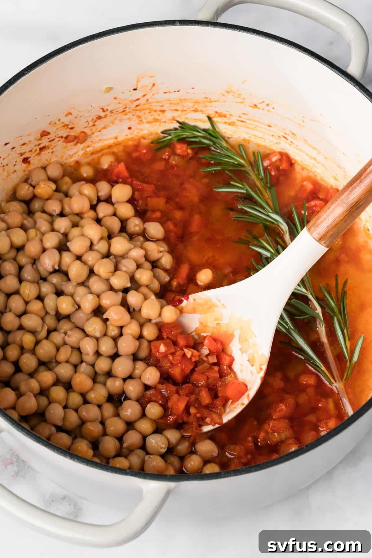 Overhead view of a white spoon stirring chickpeas into the sautéed vegetable and aromatic mixture in a pot for Pasta e Ceci.