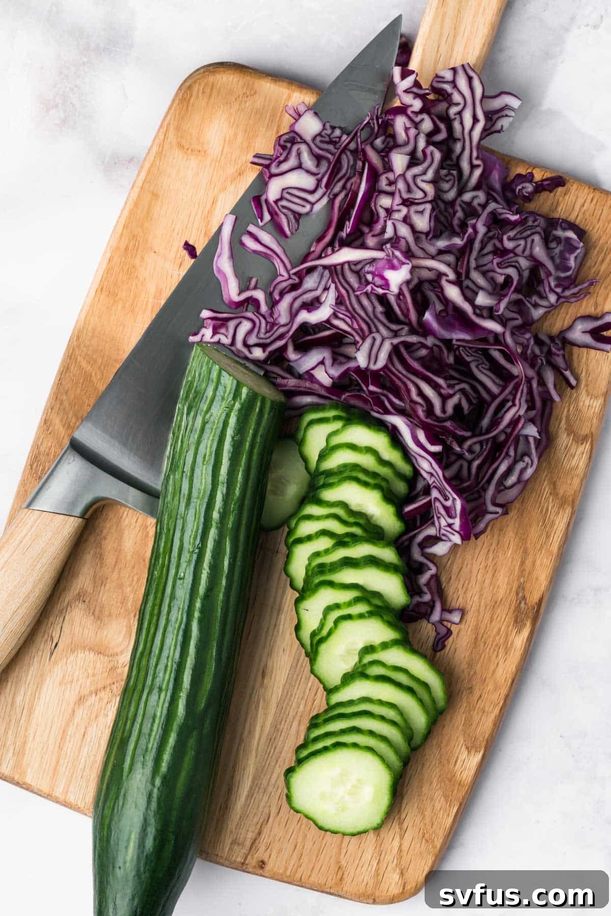 Freshly sliced cucumbers and shredded red cabbage arranged on a cutting board, ready for the bowls.