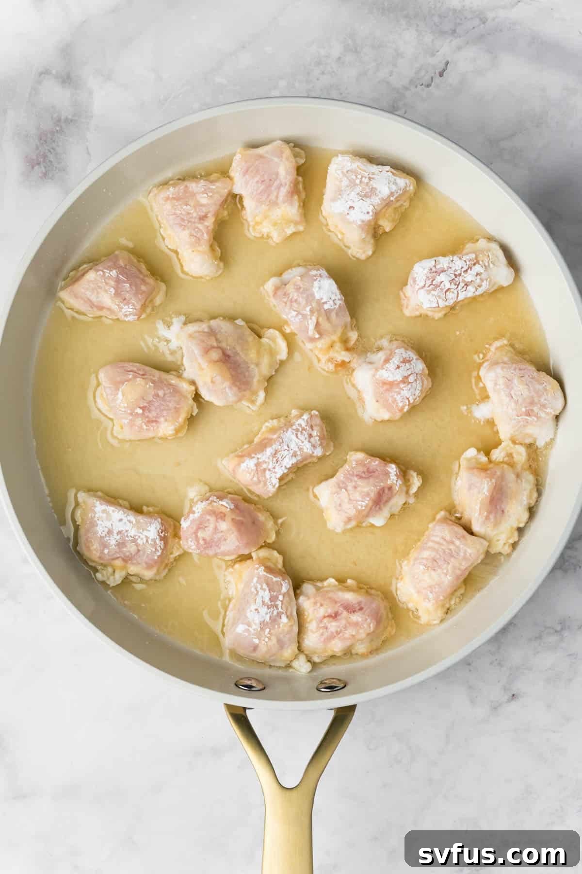 Raw, breaded chicken pieces sizzling and beginning to brown in hot oil within a skillet.