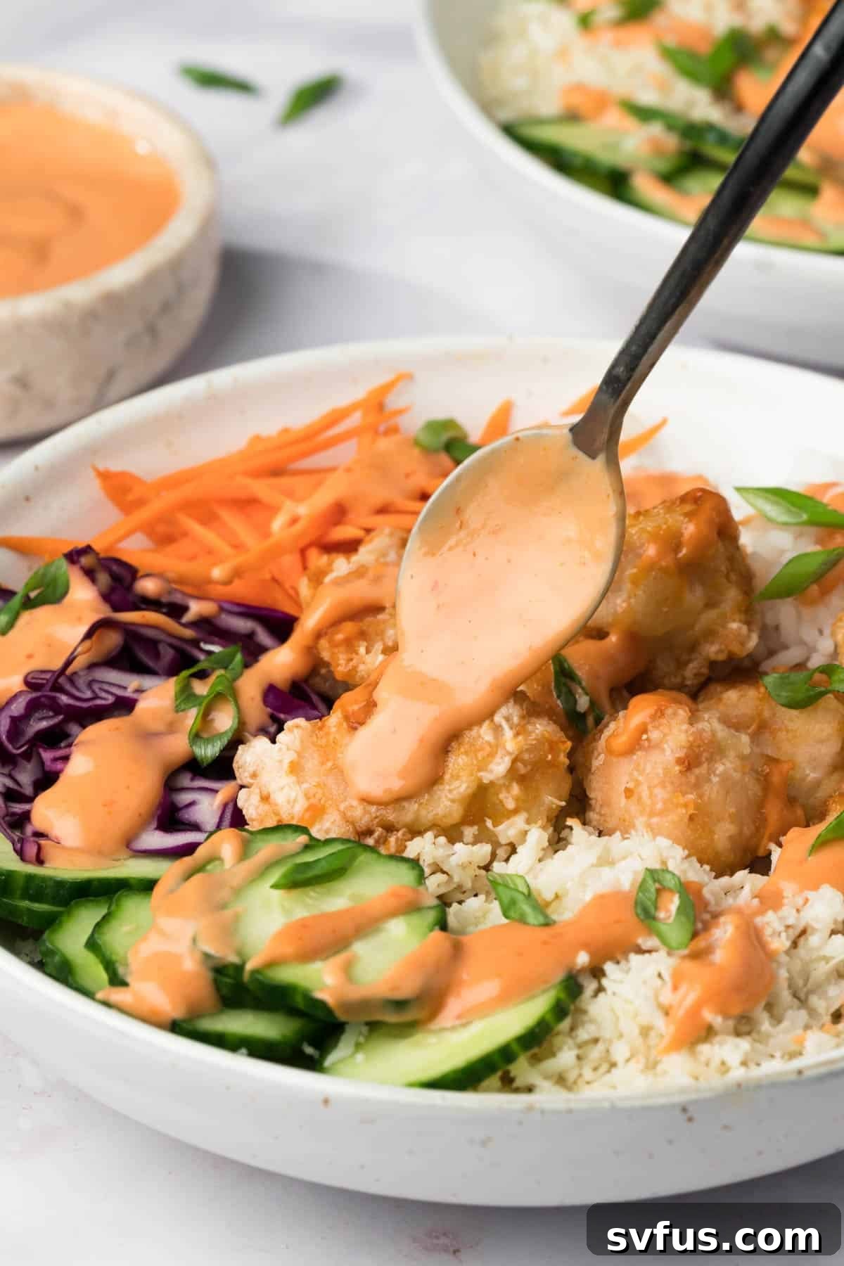 A spoon delicately drizzling creamy bang bang sauce over a freshly assembled Bang Bang Chicken Bowl, enhancing its appeal.
