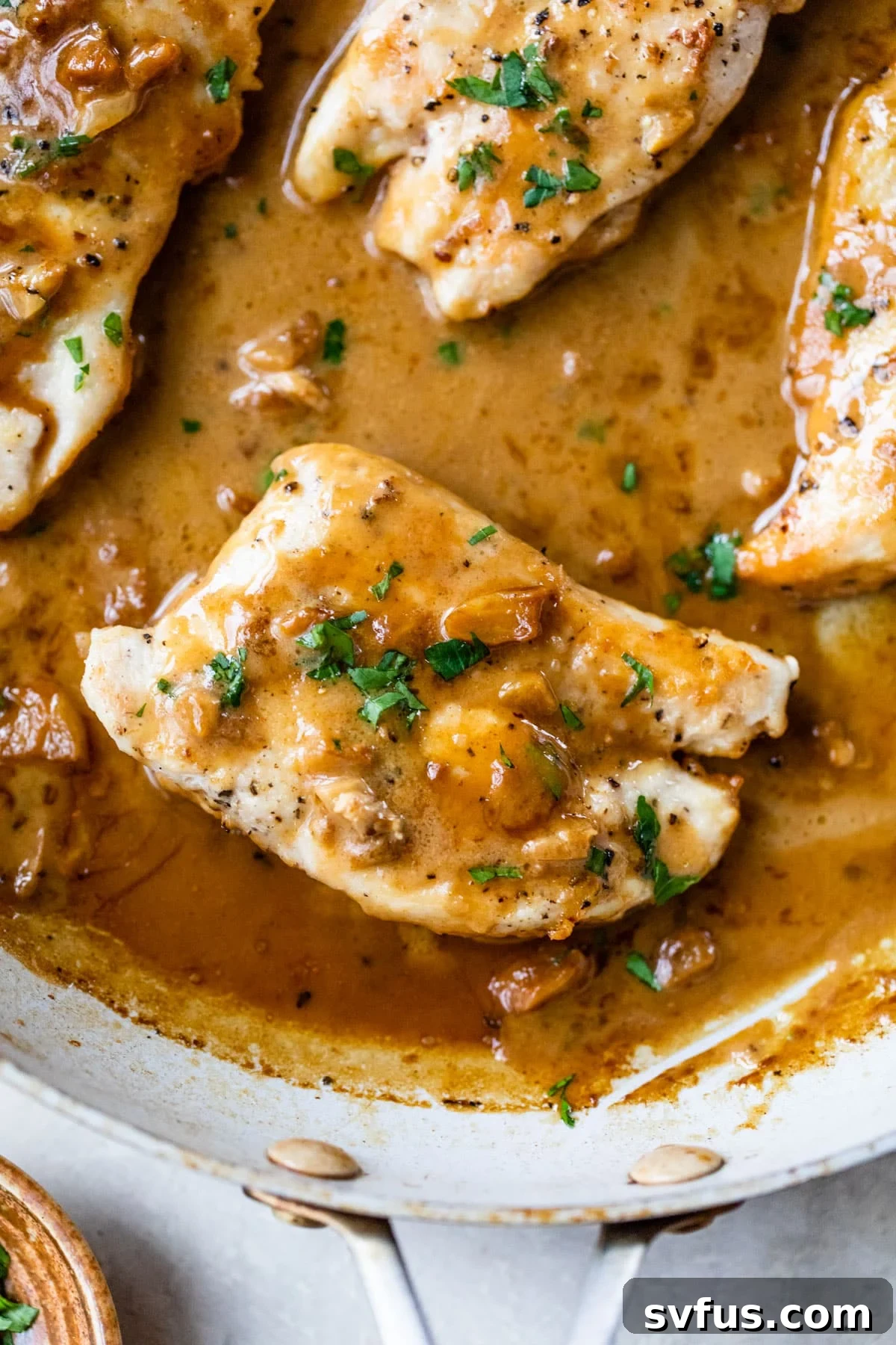 Two perfectly cooked chicken breasts nestled in a skillet, generously coated with a rich, inviting orange and brown-hued creamy garlic sauce.