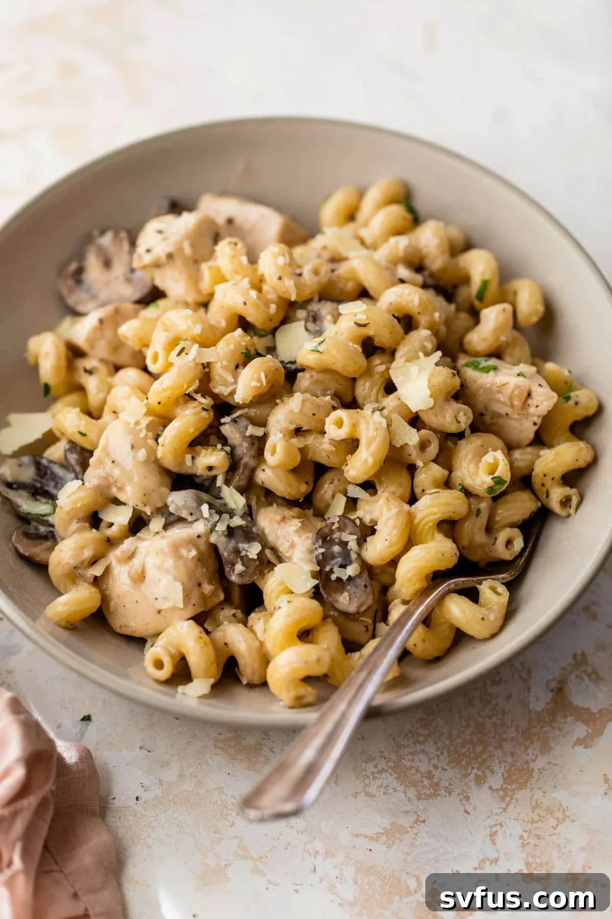 A comforting bowl of chicken mushroom pasta, garnished with freshly grated Parmesan cheese and a fork, ready to be enjoyed.