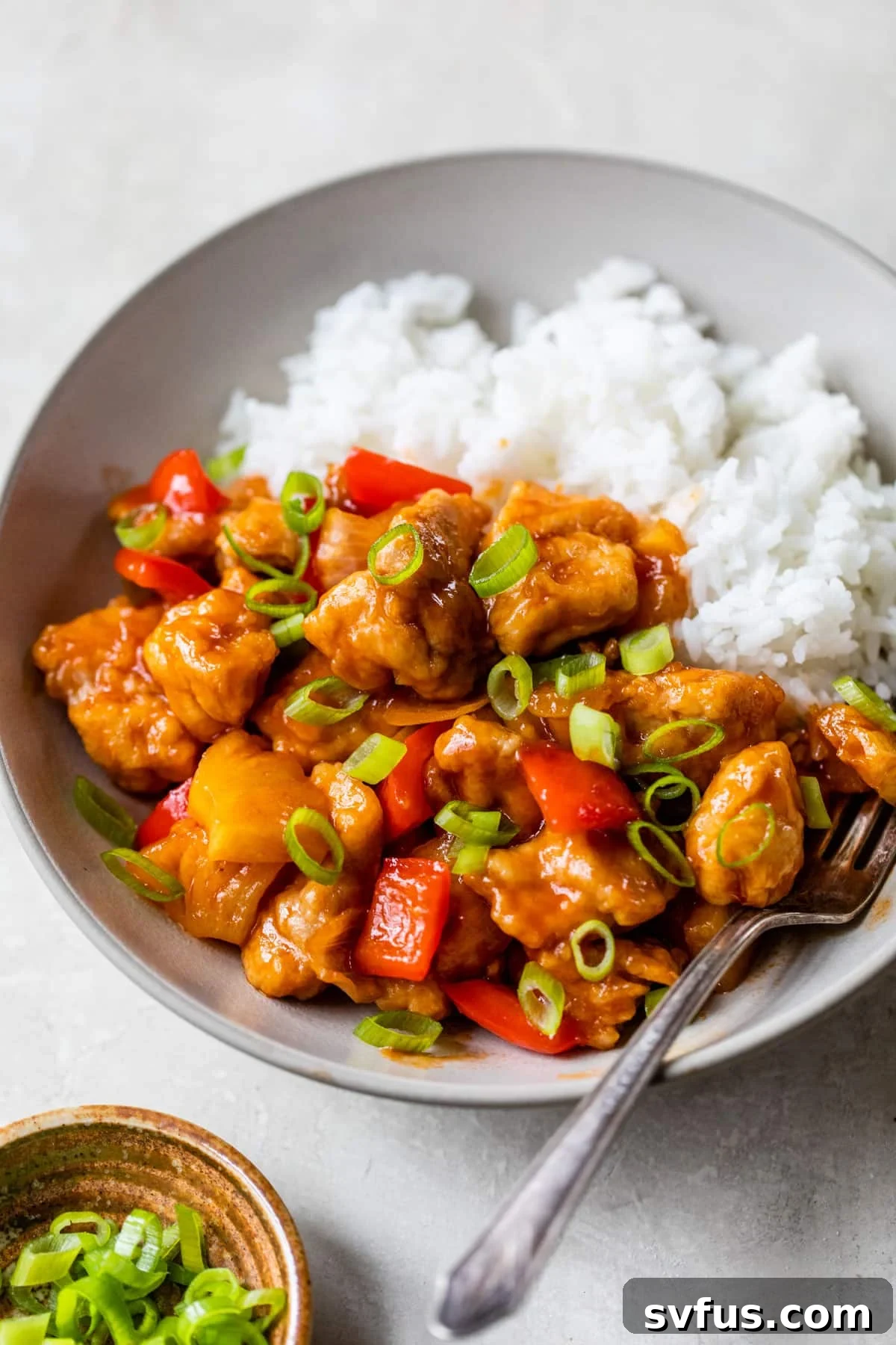 A steaming bowl of rice topped with vibrant and tender sweet and sour chicken, a healthier take on a classic favorite.