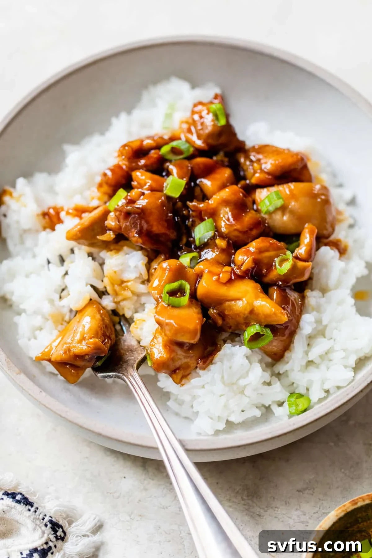 Vibrant orange glazed honey garlic chicken in a bowl, served over white rice and garnished with fresh green onions for a pop of color and flavor.