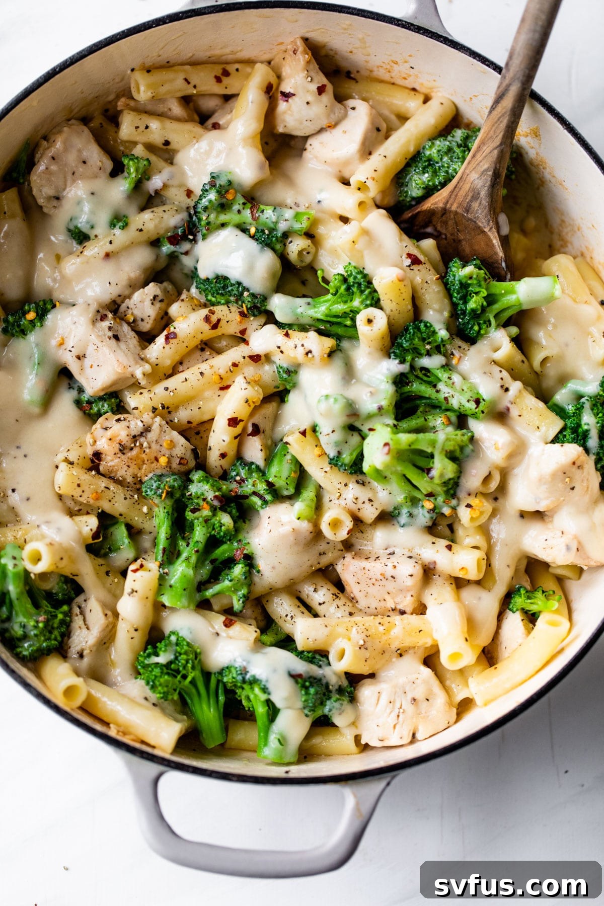 A large skillet brimming with ziti pasta, tender chicken pieces, vibrant broccoli florets, all generously coated in a creamy, healthy alfredo sauce.