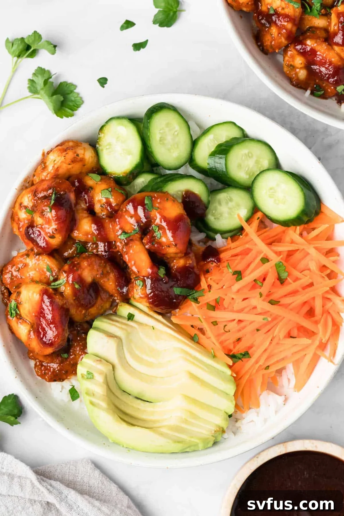 Overhead view of a vibrant BBQ Shrimp Bowl, showcasing plump, BBQ-glazed shrimp nestled on rice with fresh cucumbers, shredded carrots, and creamy avocado slices.