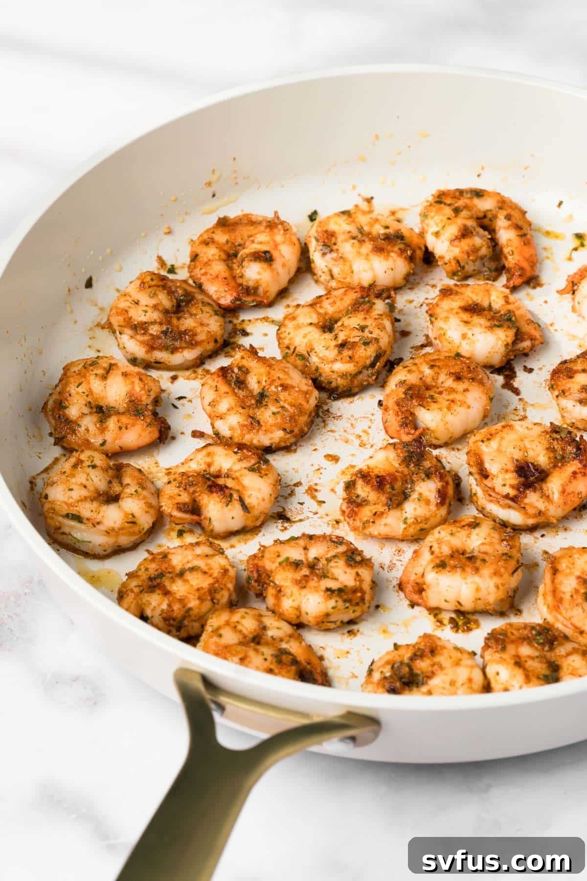 Side view of plump, pink, seared shrimp cooking in a hot skillet, showing a slight char.