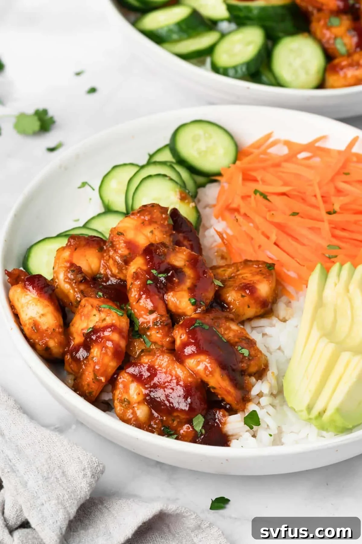 Side view of a beautifully assembled BBQ Shrimp Bowl, showcasing layers of rice, shrimp, cucumbers, carrots, and avocado.