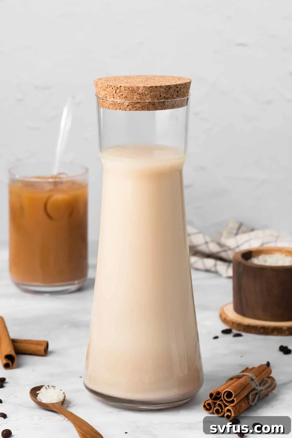 Side view of a pitcher filled with horchata, with a finished horchata latte in the background, showcasing the fresh ingredients.