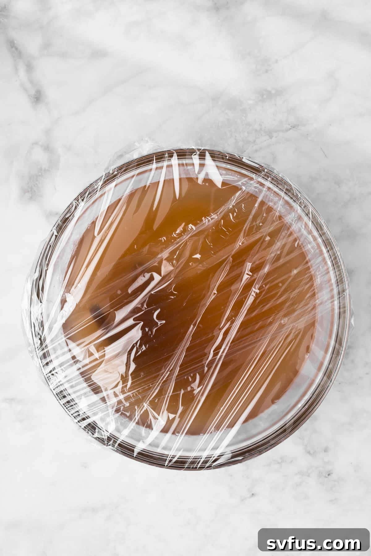 Overhead view of a plastic-covered bowl filled with white rice, water, cinnamon sticks, brown sugar, vanilla, and salt, ready for soaking.