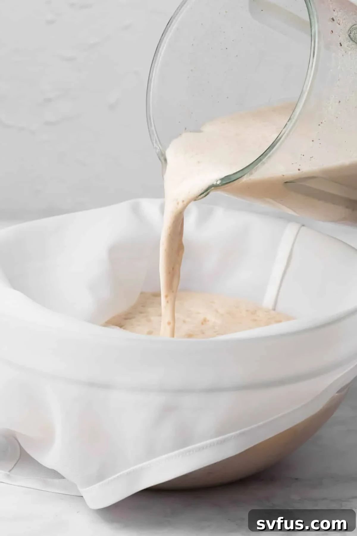 The process of pouring blended horchata through a nut milk bag into a large glass bowl to separate solids.