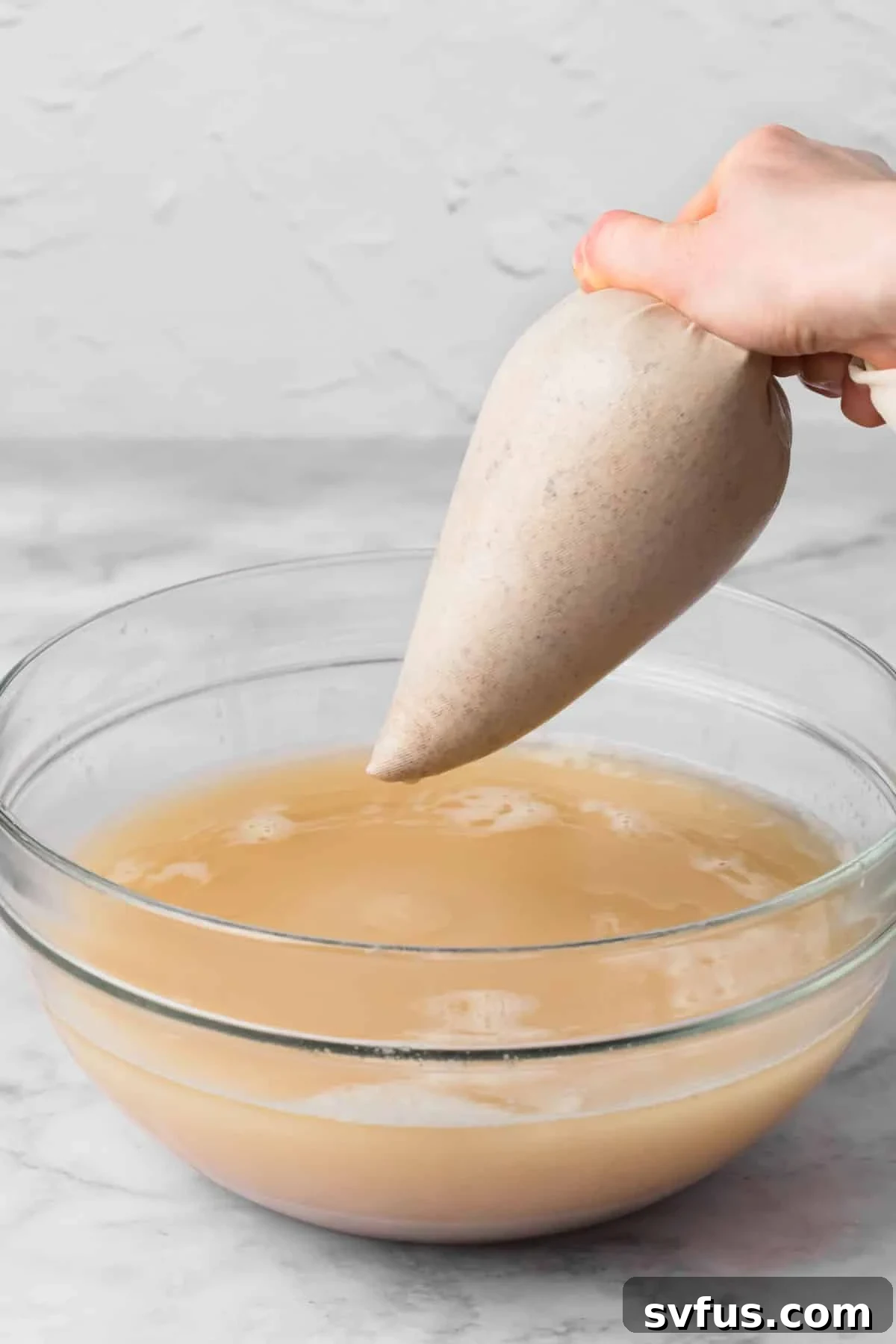 Close-up of straining blended horchata from a nut milk bag into a large glass bowl, revealing the smooth liquid.