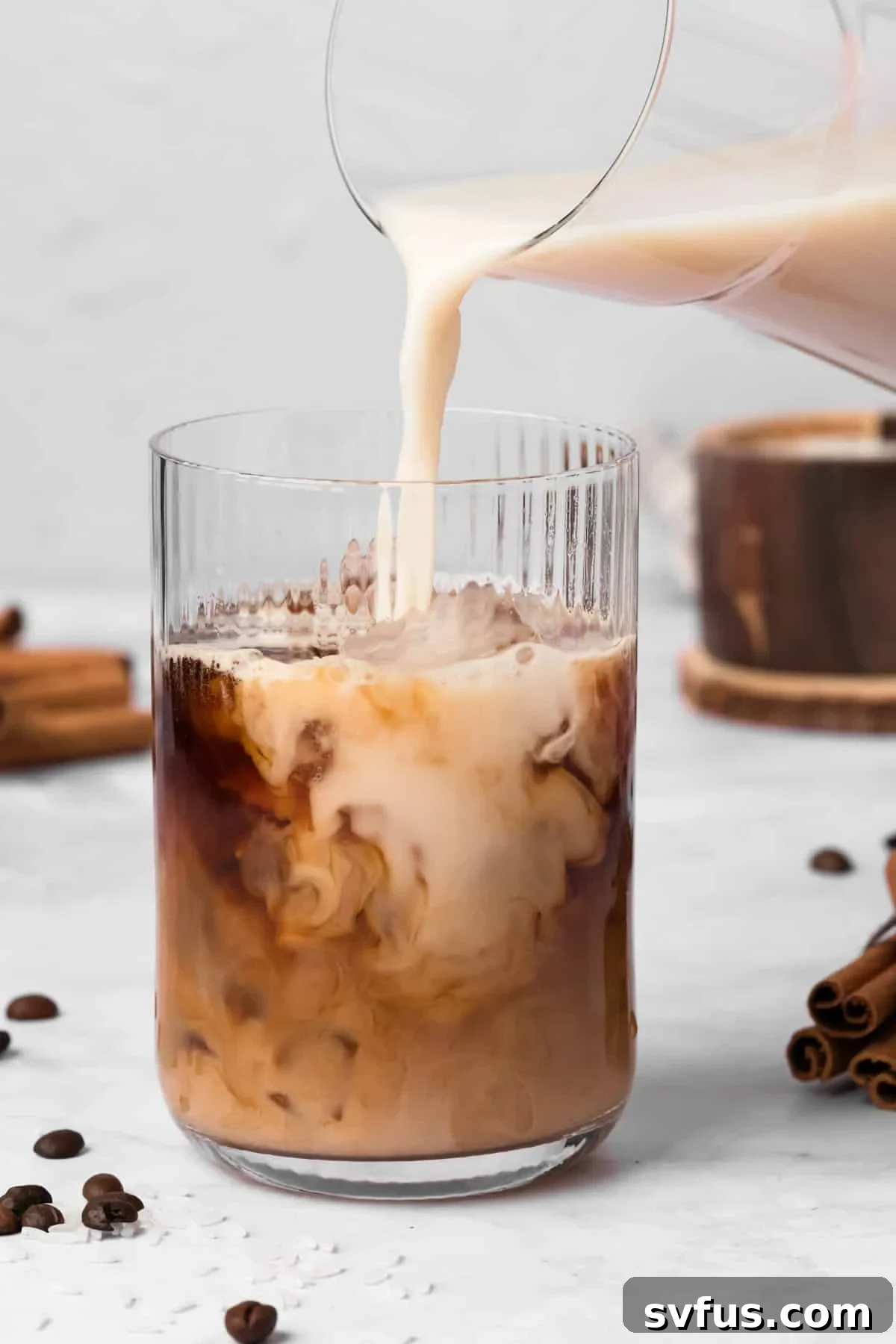 Side view of pouring creamy horchata into a glass already containing espresso and ice, forming an iced latte.