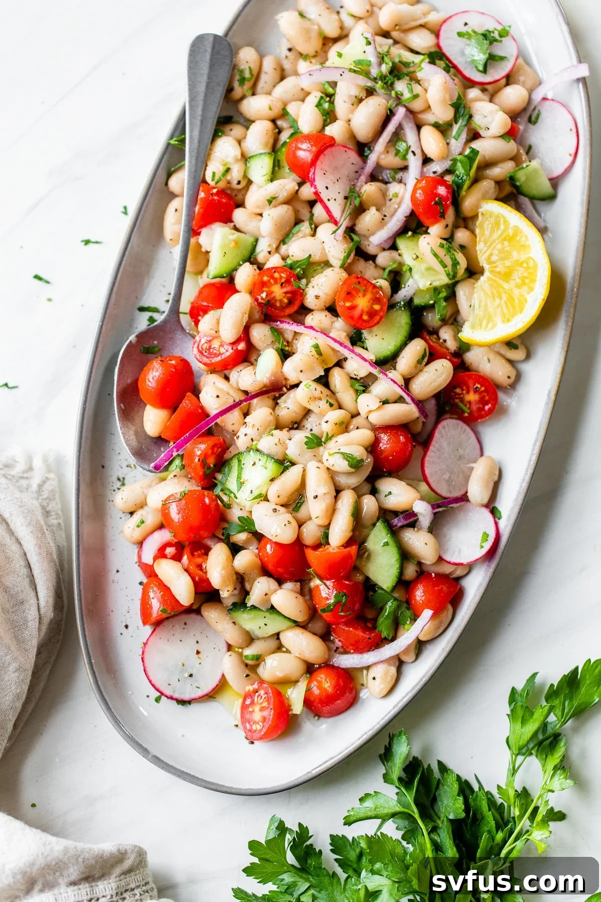 A refreshing Cannellini Bean Salad with white beans, tomatoes, and cucumbers on an oval platter.