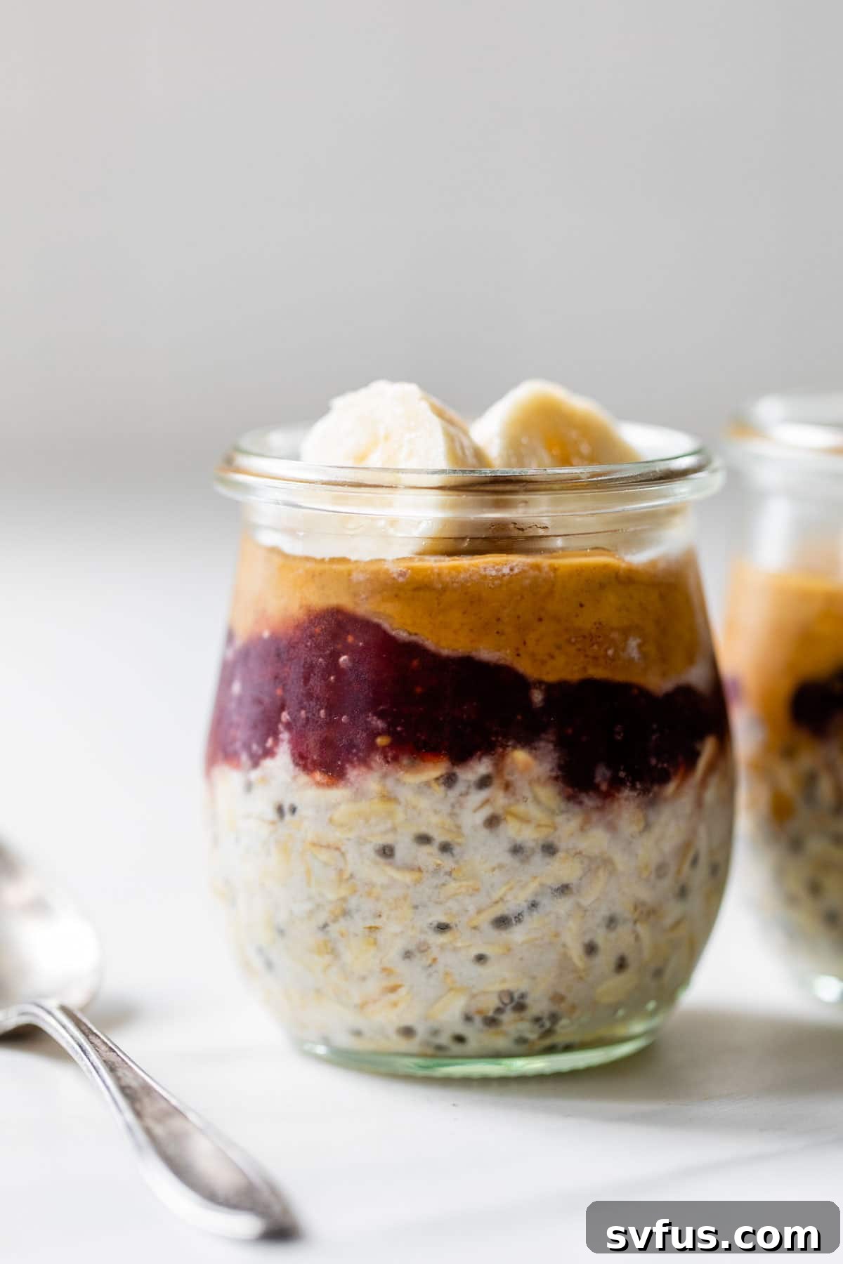 A jar of PB&J Overnight Oats, layered with oats, peanut butter, jelly, and topped with banana slices.
