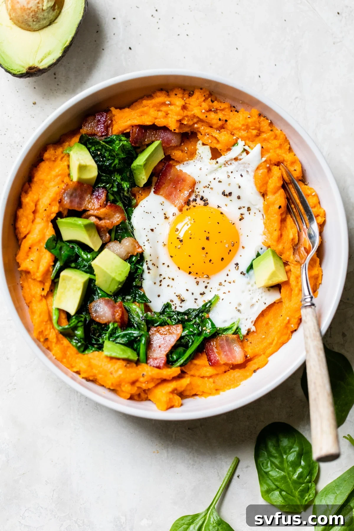A hearty Sweet Potato Breakfast Bowl topped with crispy bacon, a fried egg, fresh spinach, and creamy avocado.
