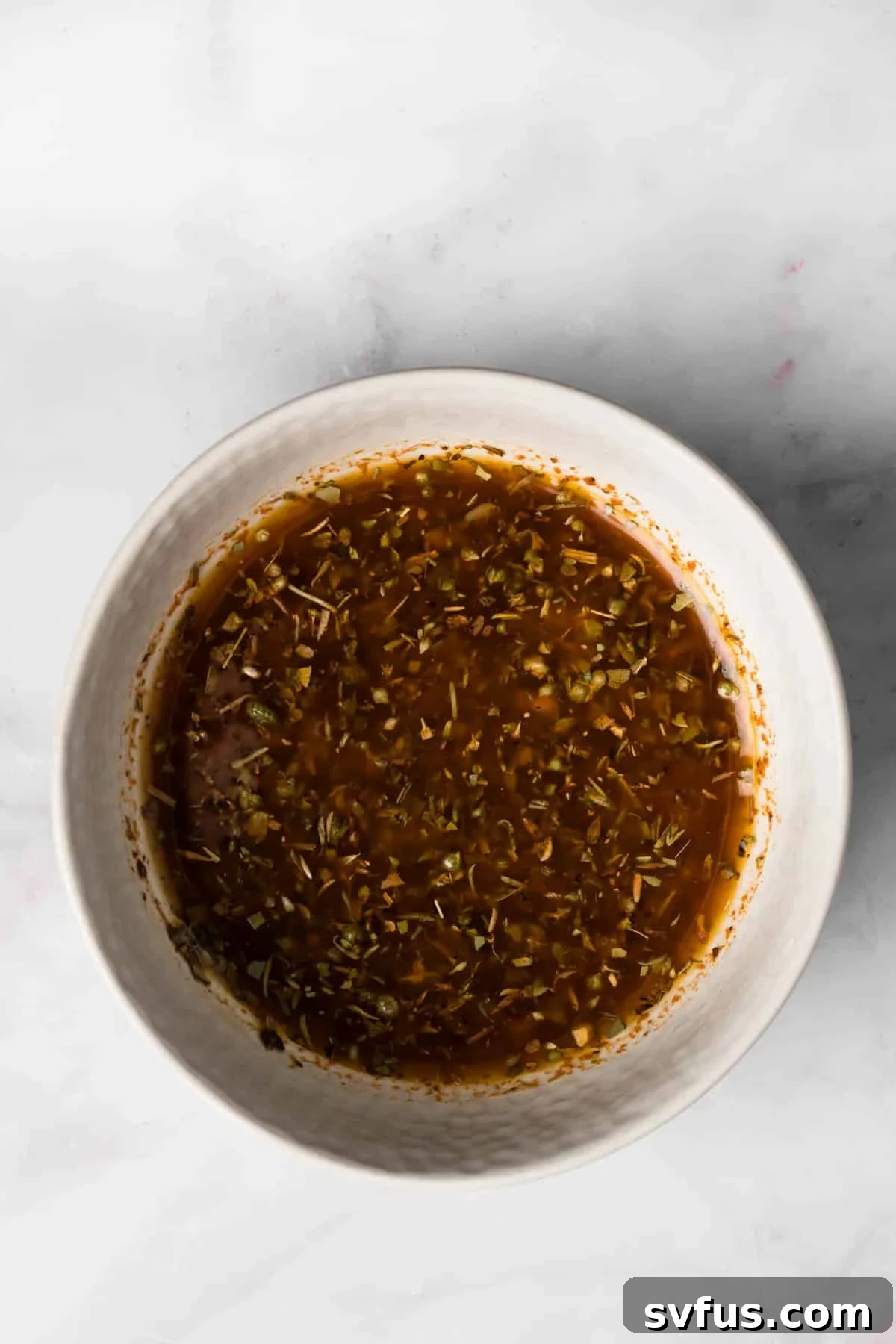 Overhead view of a small bowl filled with the vibrant lemon-garlic marinade, showing its smooth consistency and flecks of herbs, ready for the Sheet Pan Chicken and Potatoes.