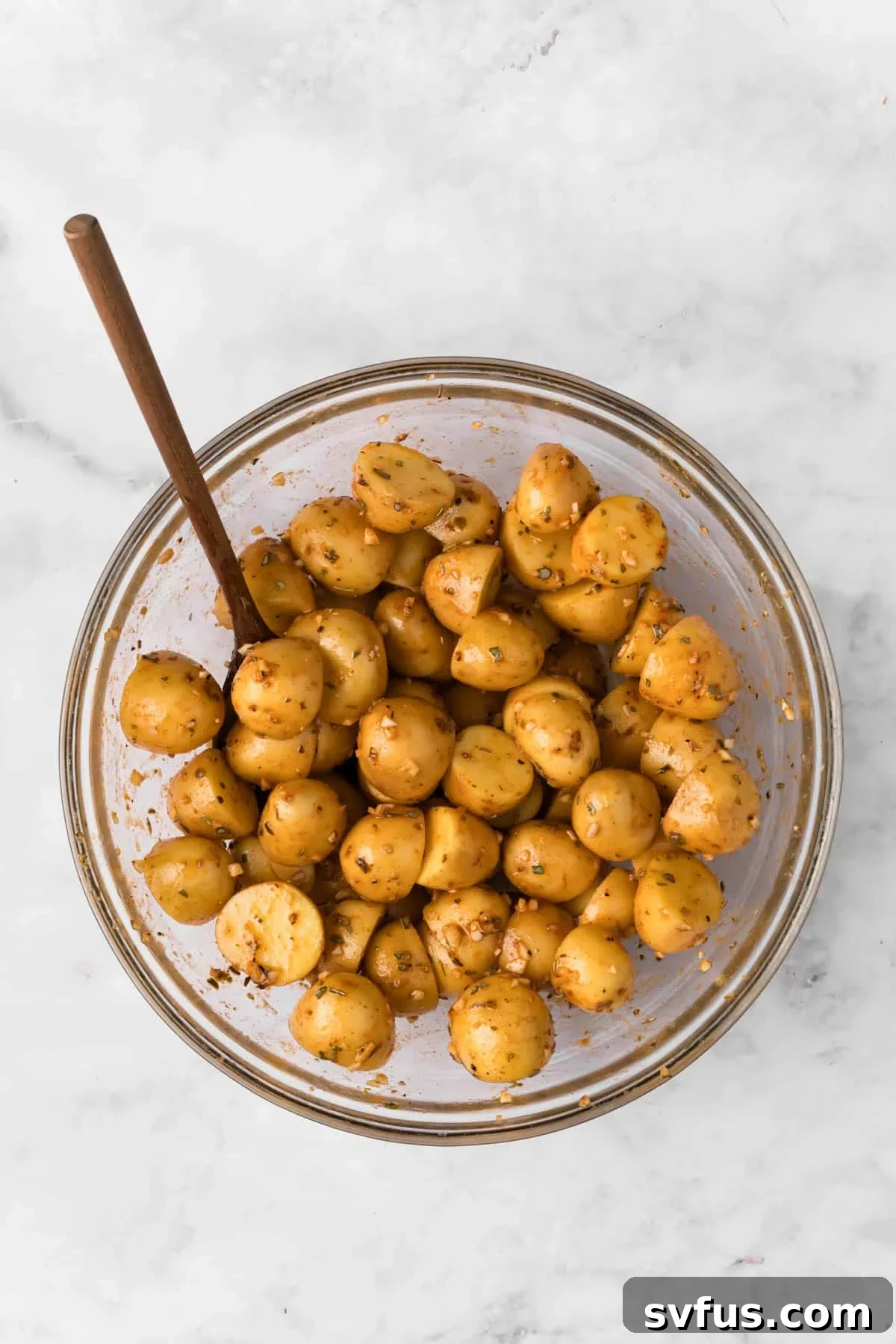 Overhead view of raw baby potatoes, perfectly seasoned and coated in the vibrant lemon-garlic marinade, held in a clear glass bowl, ready for roasting.