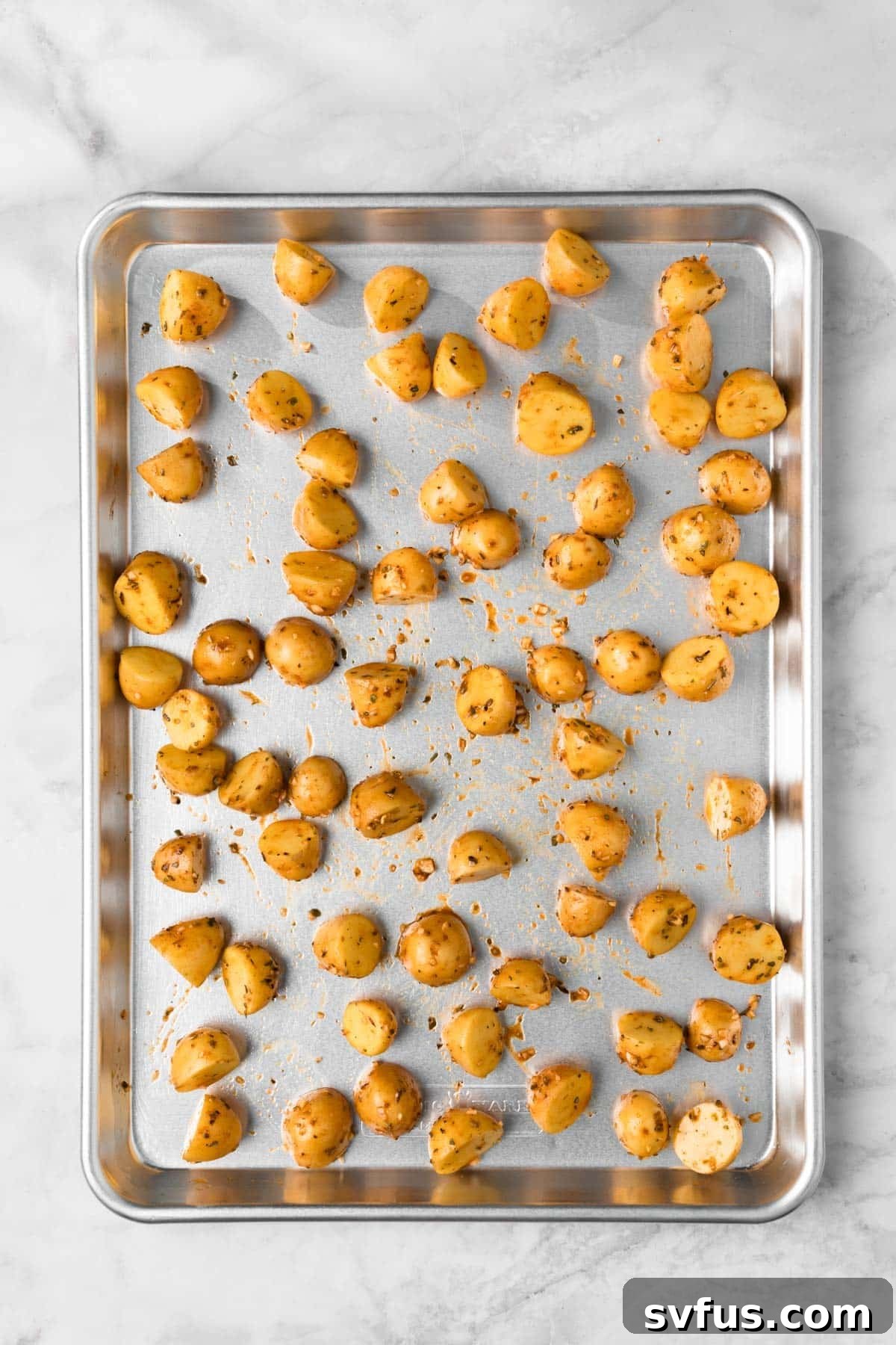 Overhead view of seasoned baby potatoes spread in a single, even layer on a sheet pan, ready for their initial roast in the oven.
