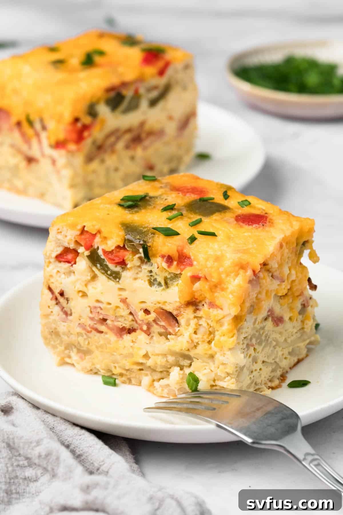 A delicious slice of Crockpot Breakfast Casserole on a plate, showcasing fluffy eggs, crispy hashbrowns, and savory bacon, garnished with chives.