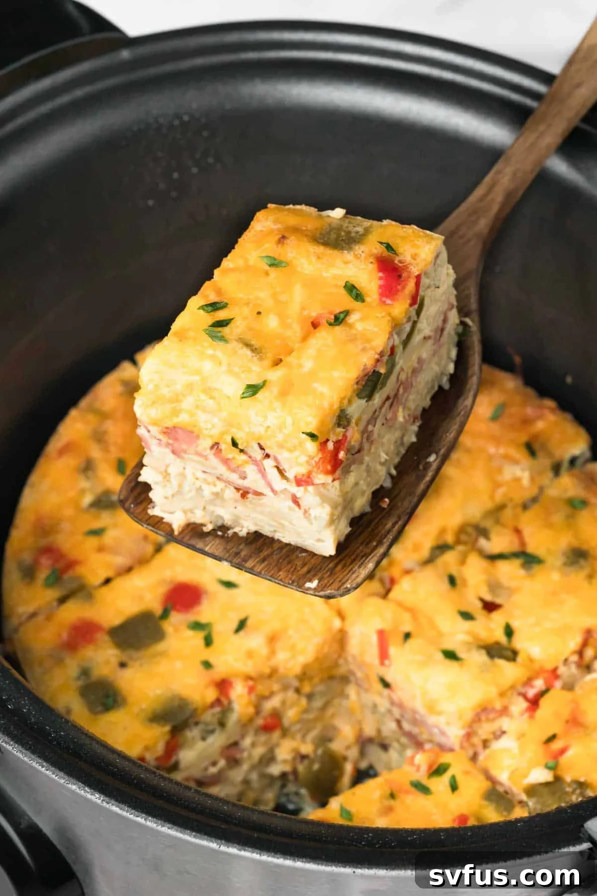 Side view of a wooden spoon lifting a perfectly cooked, golden-brown slice of crockpot breakfast casserole from the slow cooker, ready to be served.