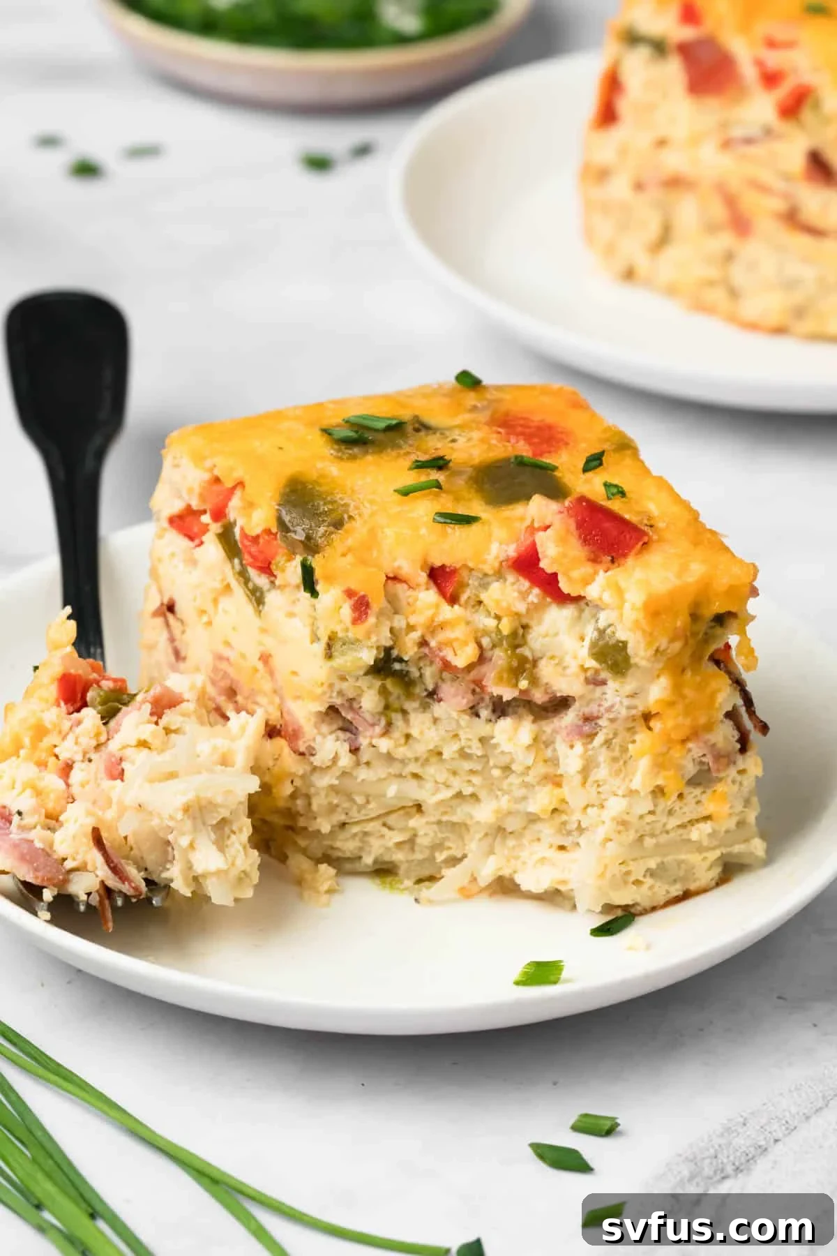 Side view of a fork cutting into a fluffy slice of crockpot breakfast casserole on a white plate, ready to be enjoyed.