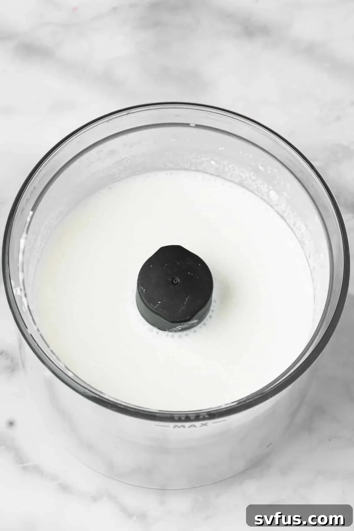 Overhead view of cottage cheese and milk being blended until smooth in a small, compact blender.