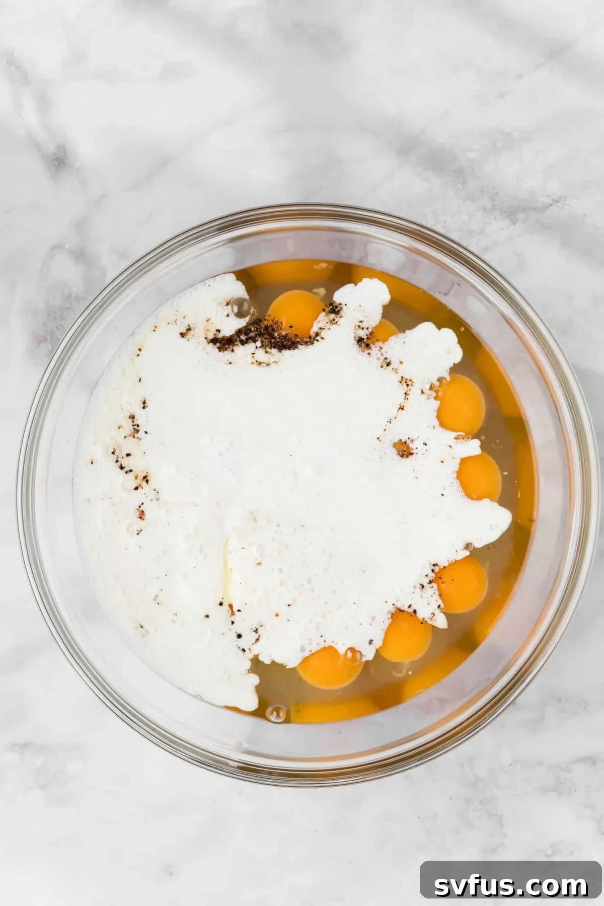 Overhead view of whisked eggs and the blended cottage cheese mixture in a large glass bowl, ready for combining.