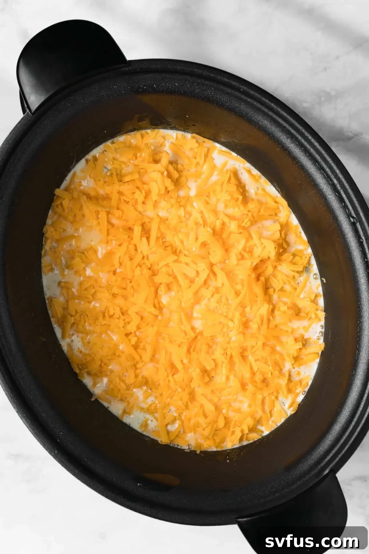 Overhead view of shredded cheese generously sprinkled over the liquid eggs and other ingredients in the crockpot, prior to cooking.