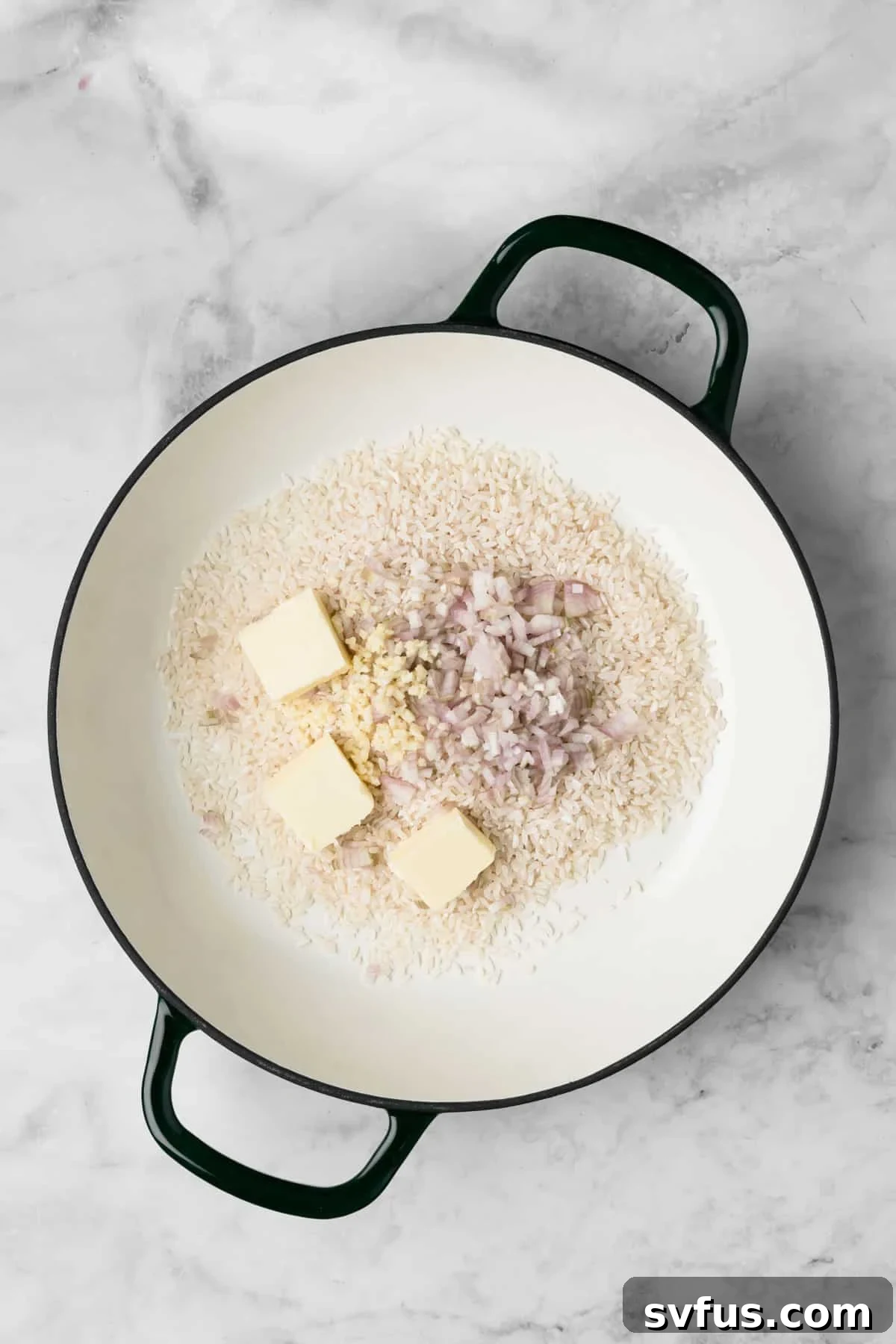 Overhead view of Arborio rice, minced garlic, diced shallots, and butter in a pot before adding broth for baked risotto.