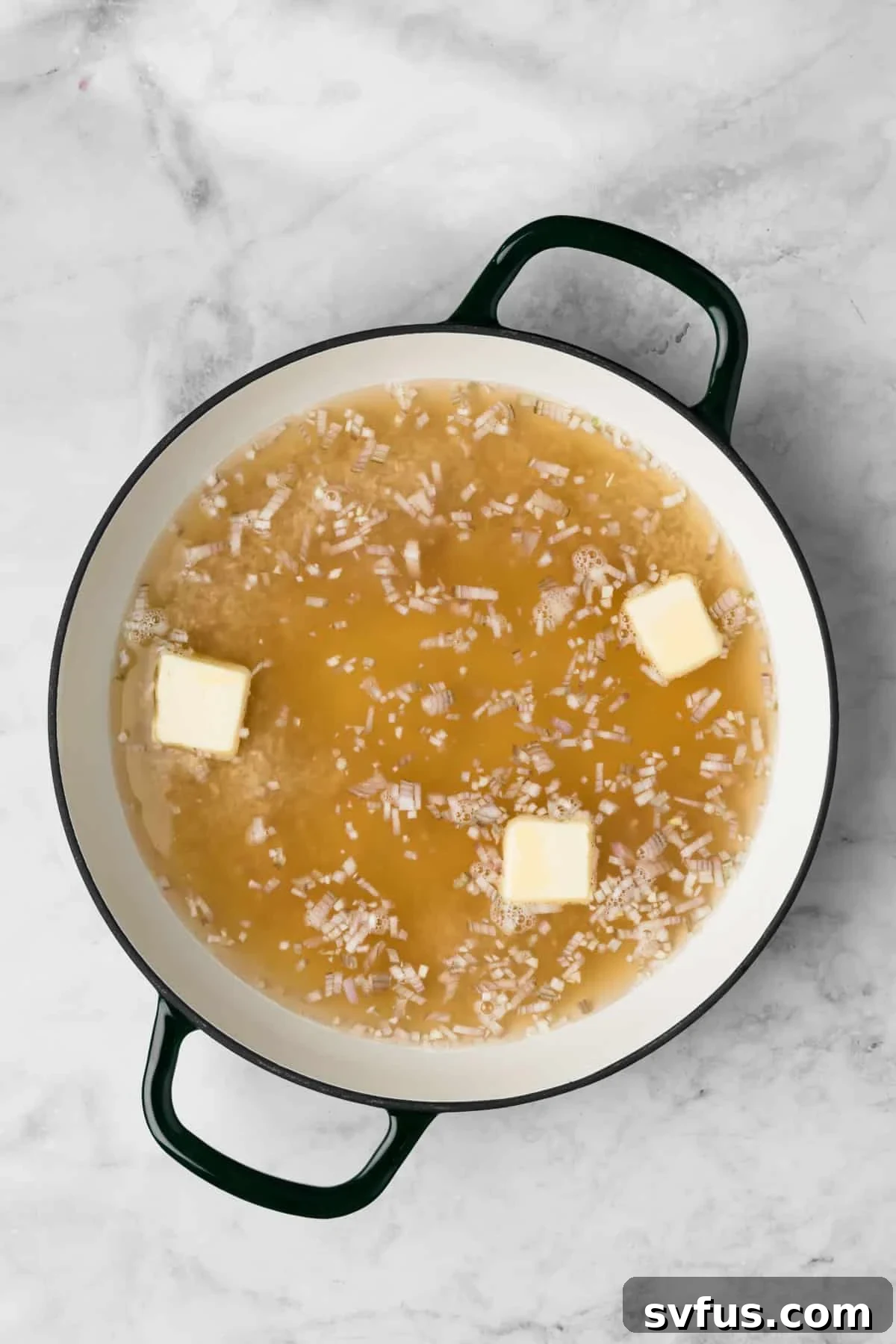 Overhead view of warm broth being added to the rice, shallots, and butter in an oven-safe pot for baked risotto.