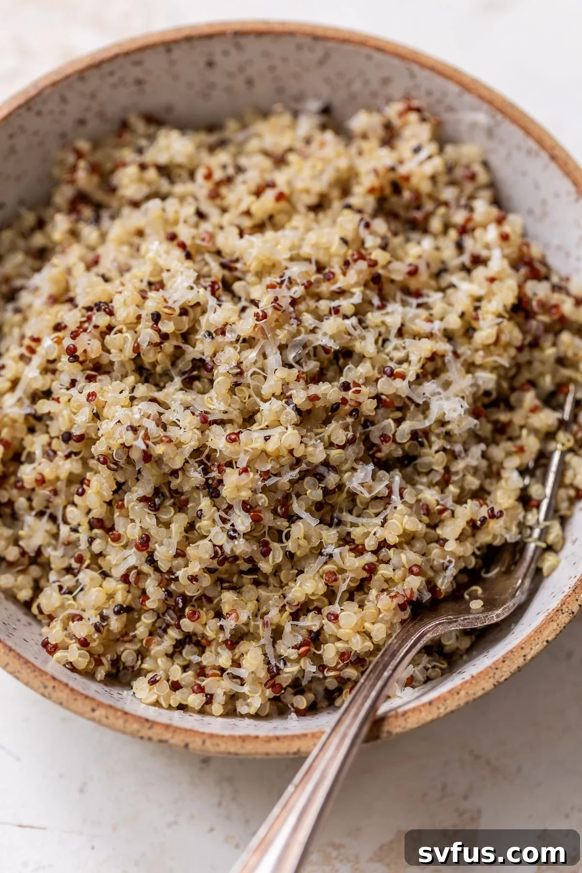 Overhead view of perfectly cooked, fluffy quinoa in a ceramic bowl with a fork, ready to be enjoyed.