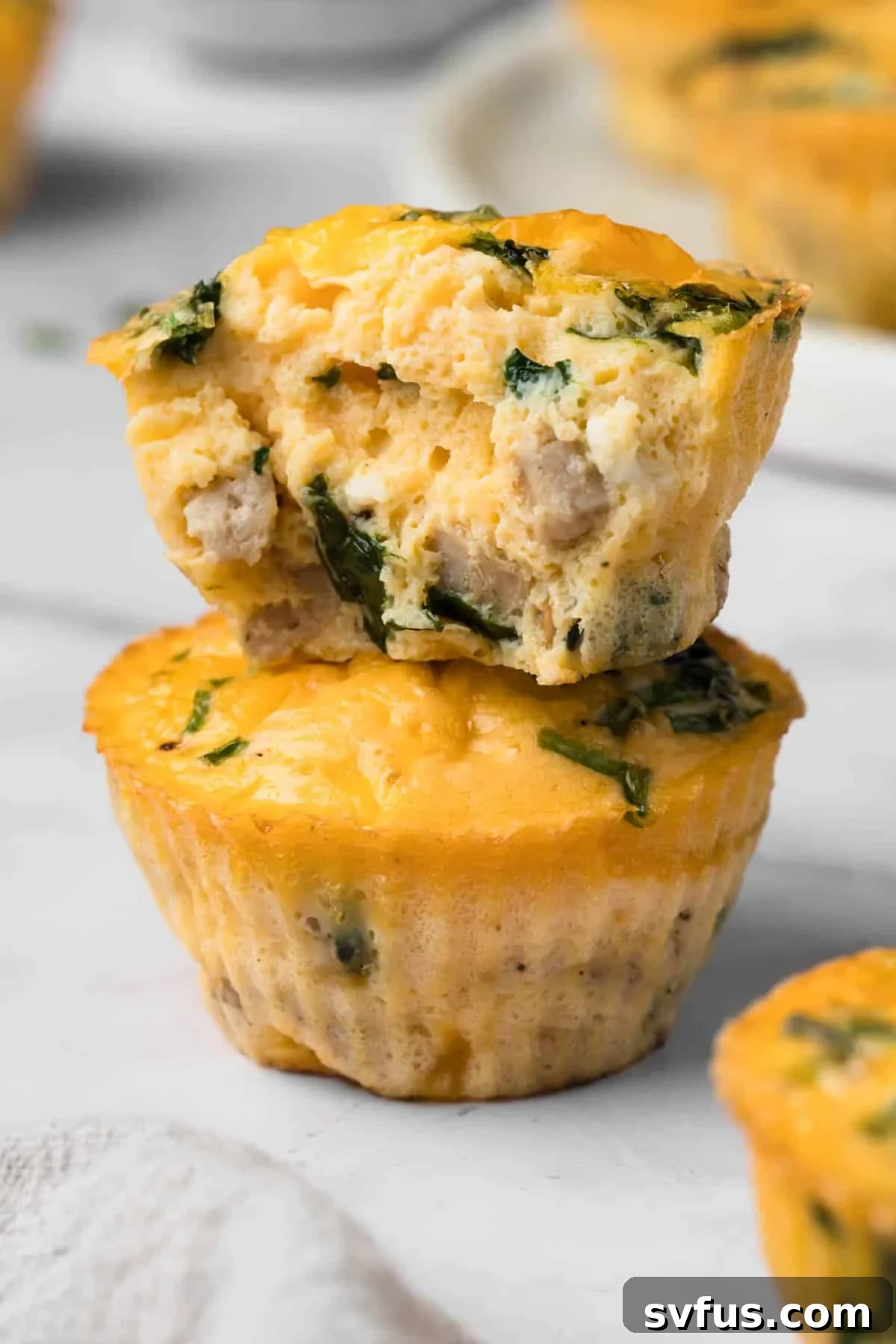 a stack of 2 egg muffins, with the top muffin ripped in half.