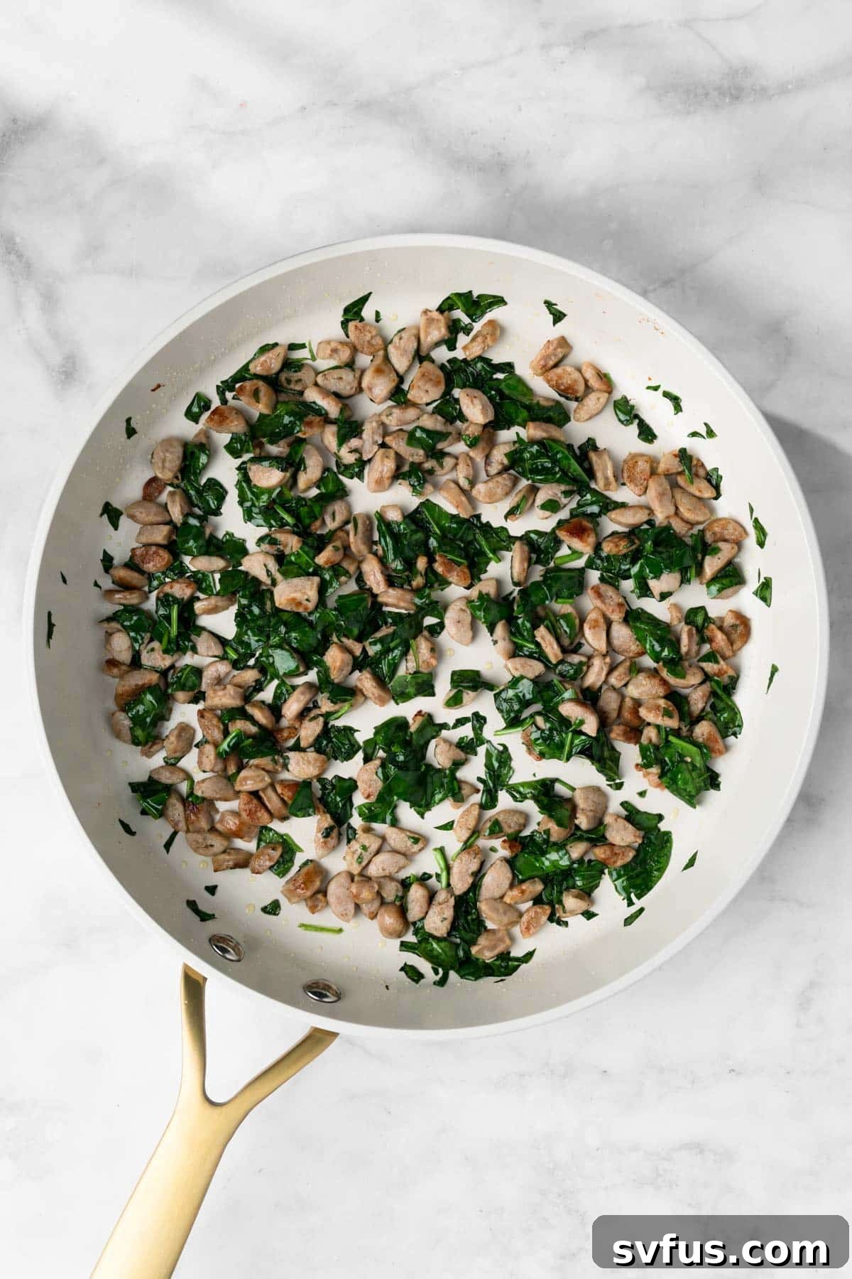Overhead view of cooked spinach and sausage in a large skillet.