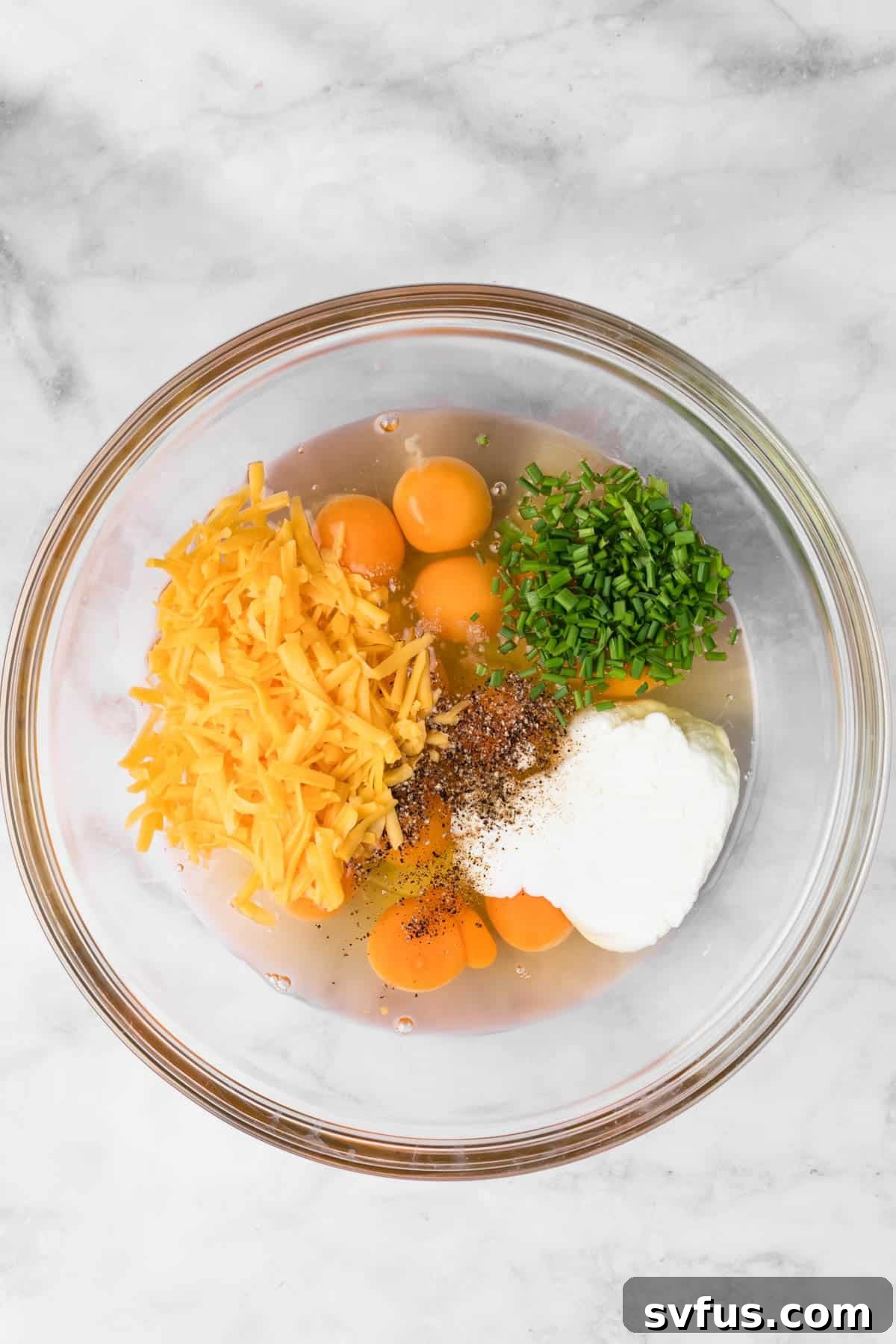 Overhead view of the ingredients for high-protein egg muffins in a glass bowl.