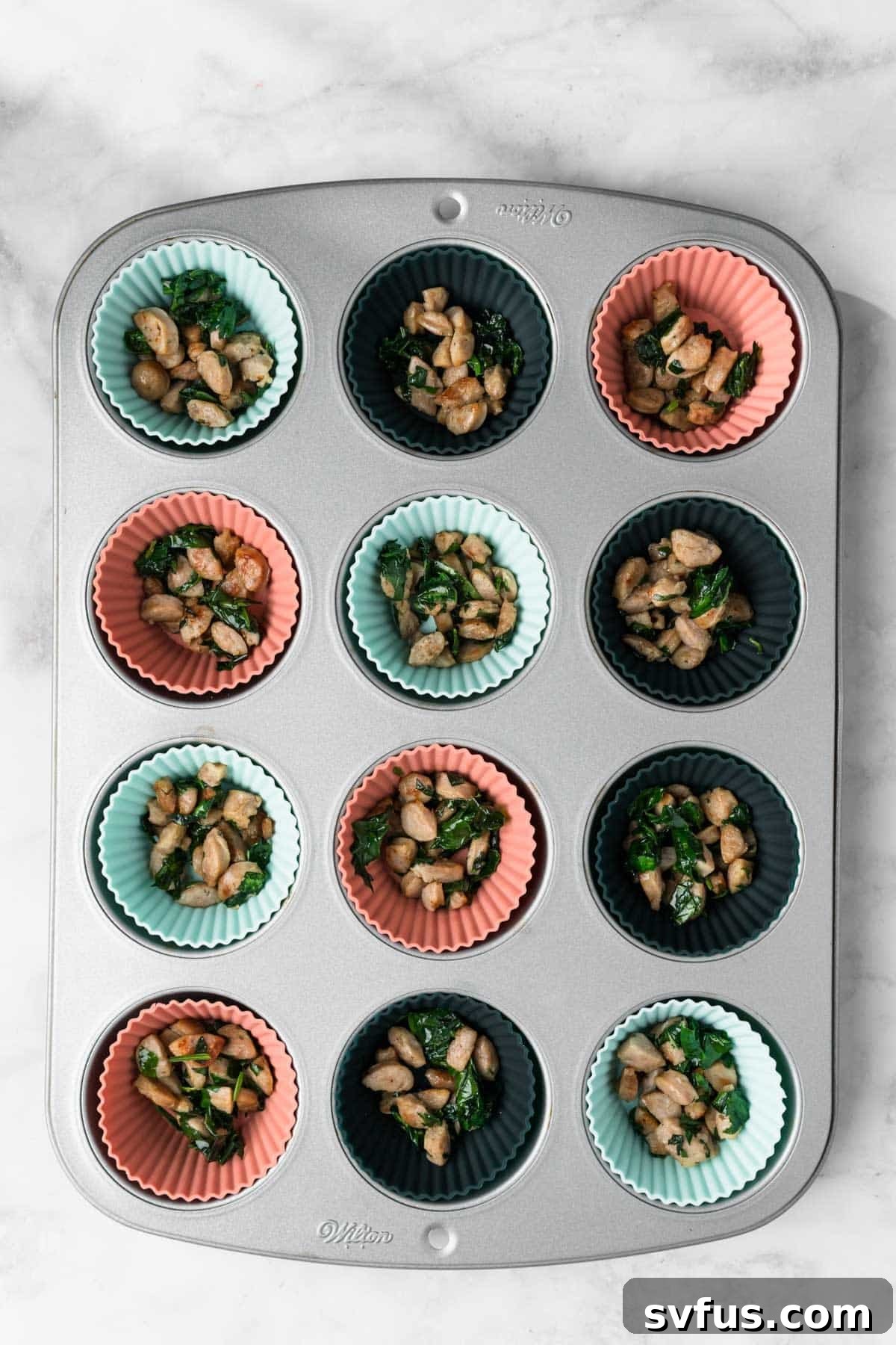 Overhead view of cooked sausage and spinach in a muffin tin.