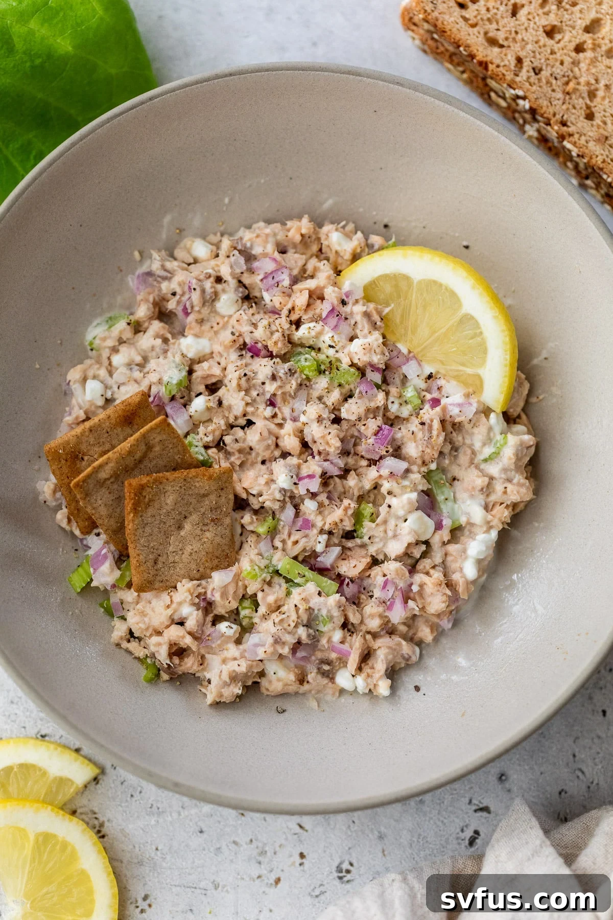 a bowl of salmon salad topped with a lemon wedges and crackers.