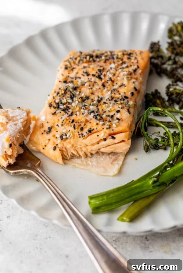 close up on a fork taking a bite out of an everything bagel salmon filet on a white plate.