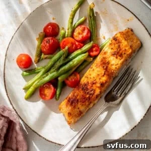 overhead view of a roasted salmon fillet on a plate with roasted green beans and tomatoes.