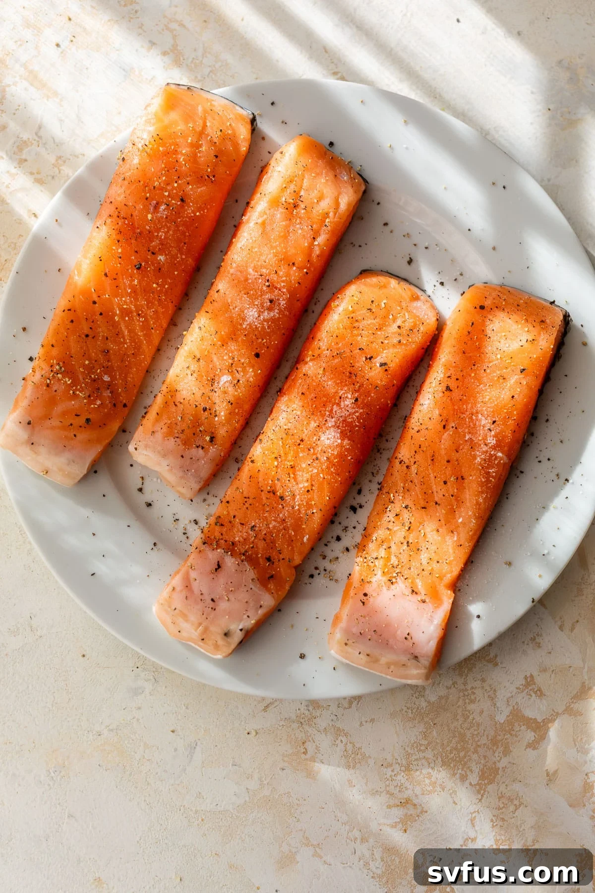 overhead view of 4 seasoned raw salmon fillets on a plate.