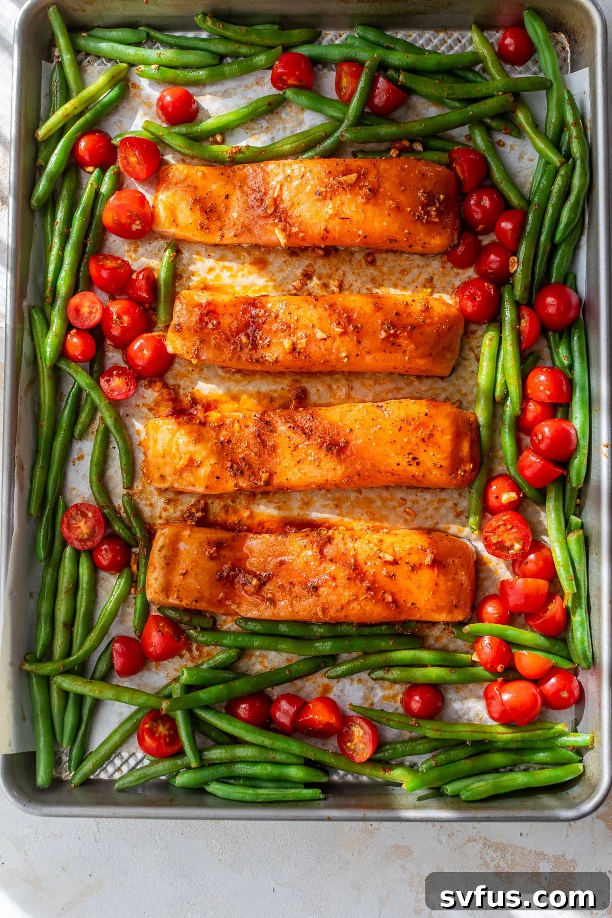 overhead view of raw salmon fillets, green beans, and tomatoes on a sheet pan.