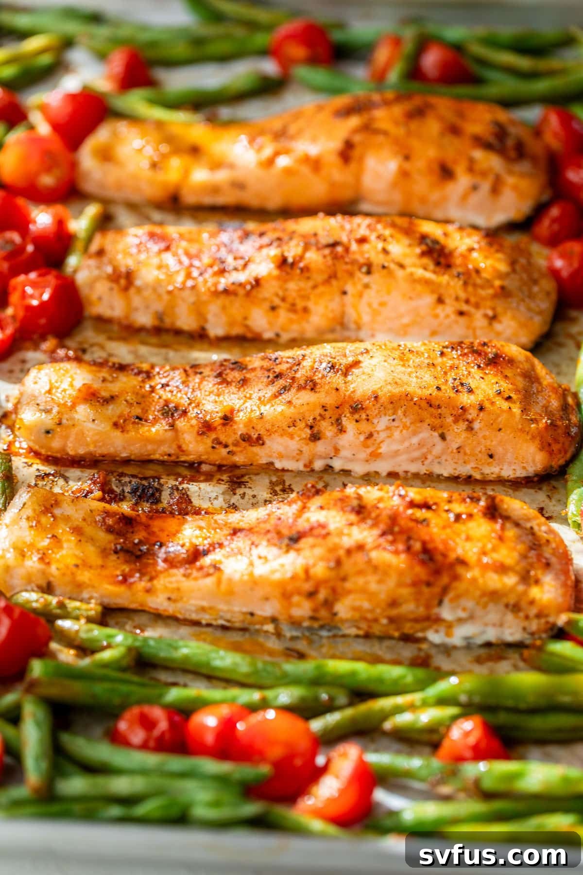 side view of roasted salmon fillets, green beans, and tomatoes on a sheet pan.